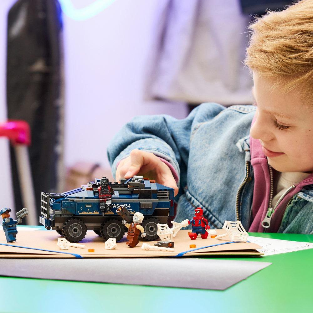 Junge spielt mit Lego Spider-Man Set: blaues Fahrzeug, Spider-Man, Bösewicht, Polizei.