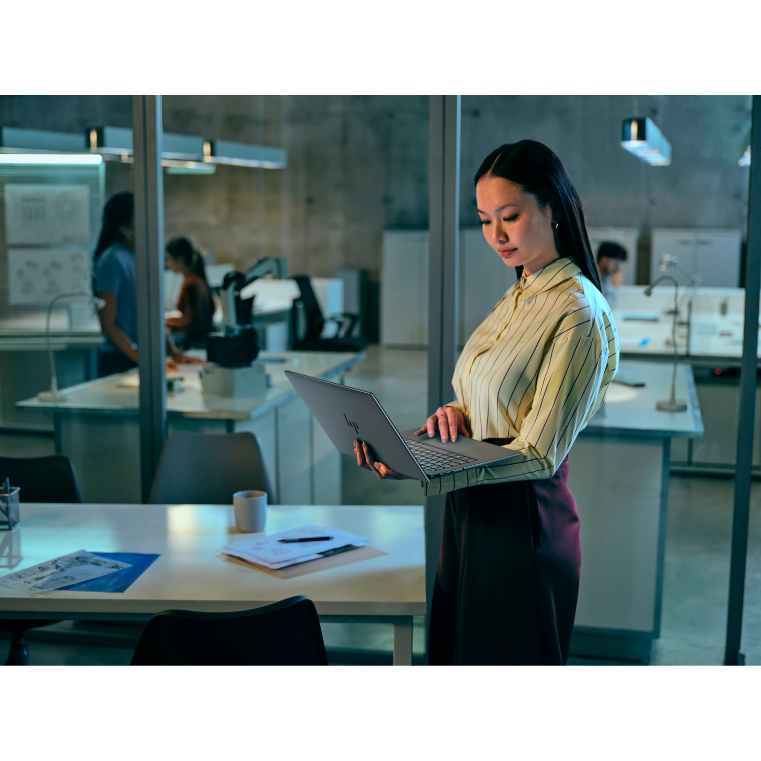 Een vrouw met lang haar houdt een laptop vast in een modern kantoor.