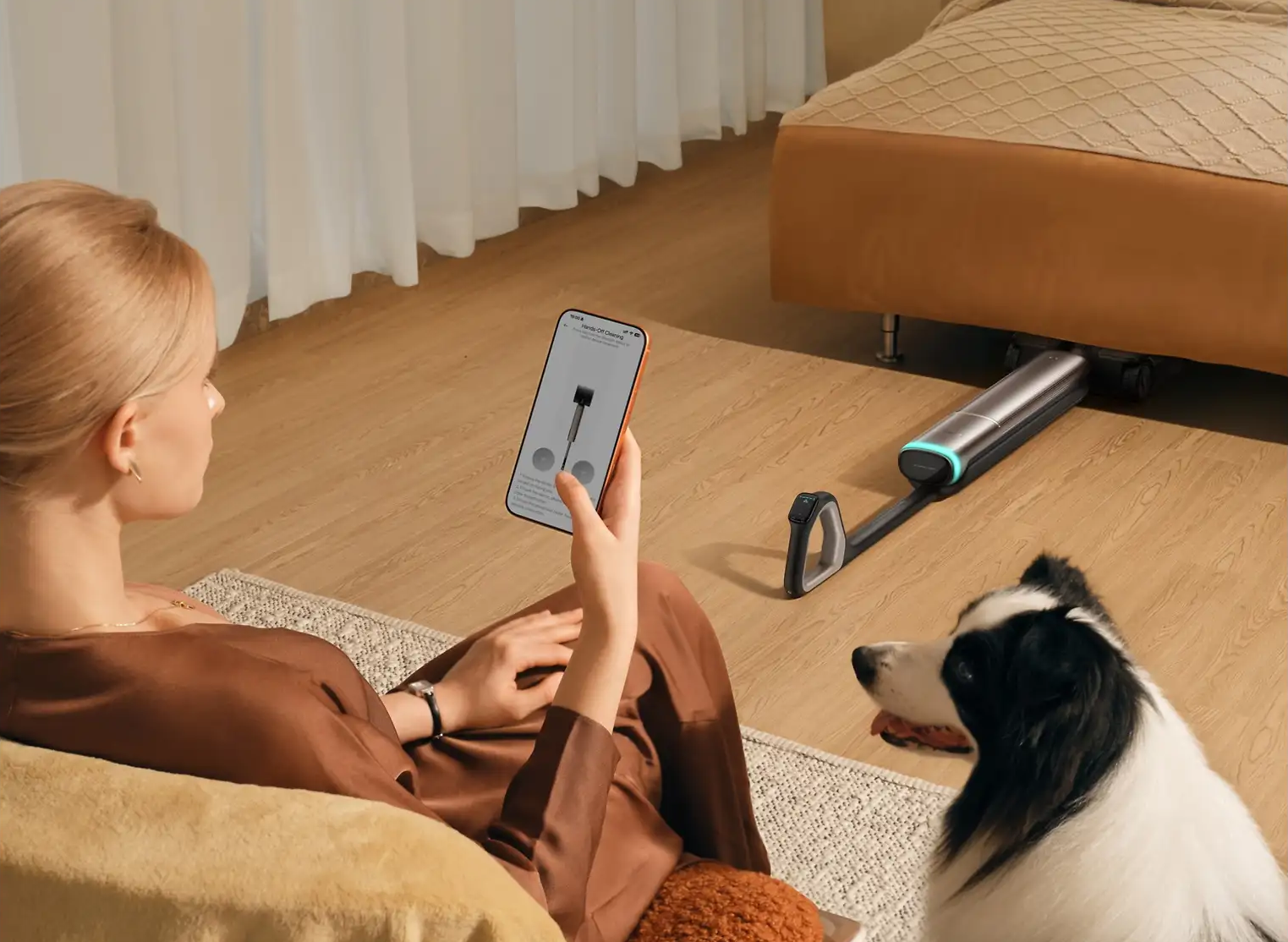 Donna tiene telefono, aspirapolvere sotto il letto, cane vicino.