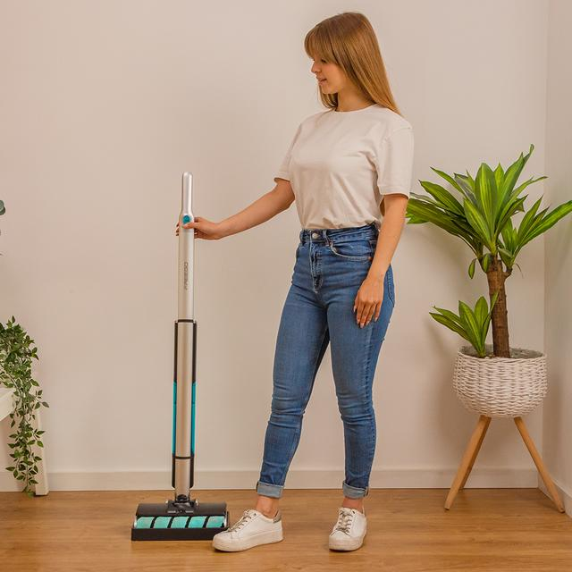 Kot pantolonlu bir kadın, bitkilerin olduğu bir odada kablosuz elektrikli süpürgenin yanında duruyor.