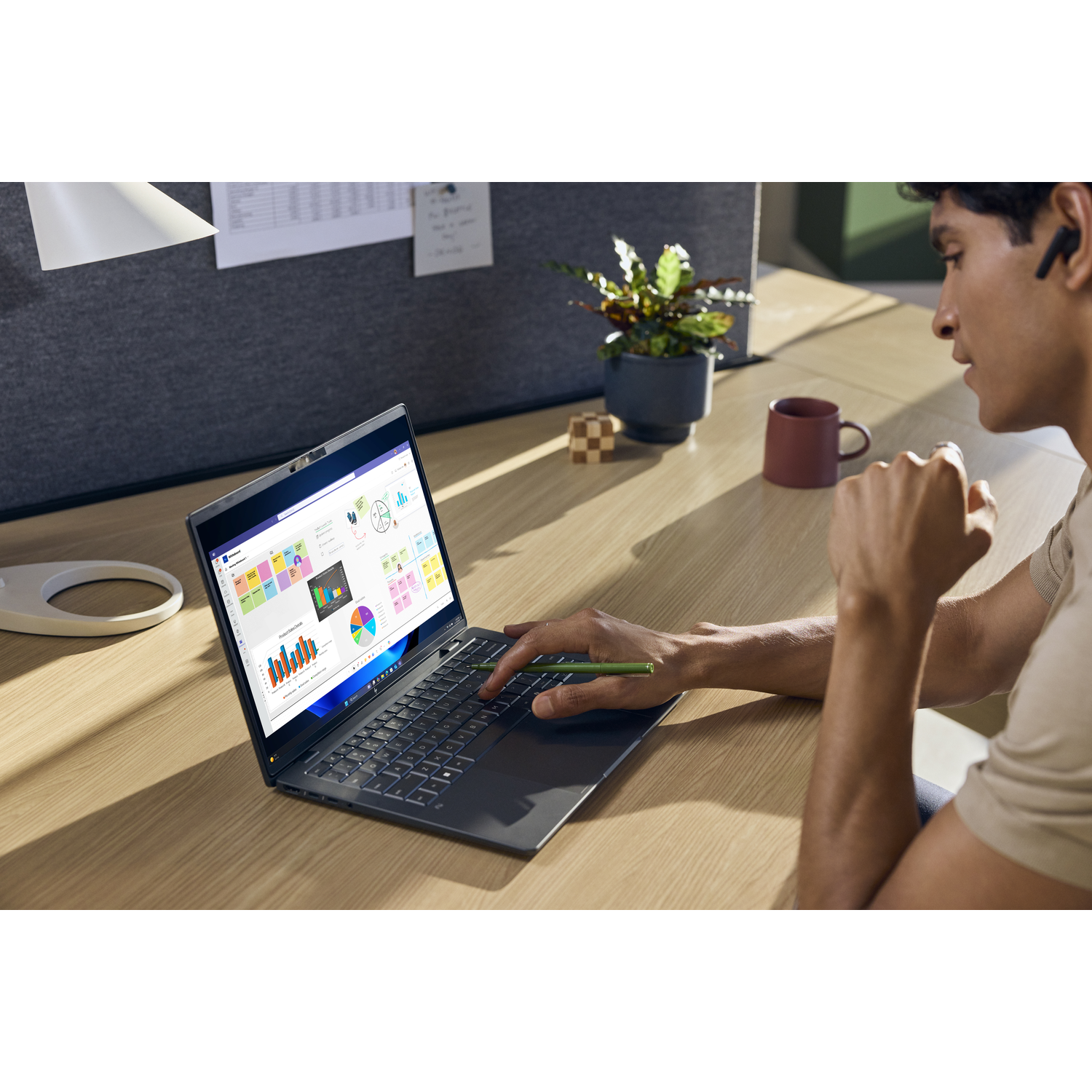 Man gebruikt laptop met grafieken. Bureau heeft plant, mok, puzzel.