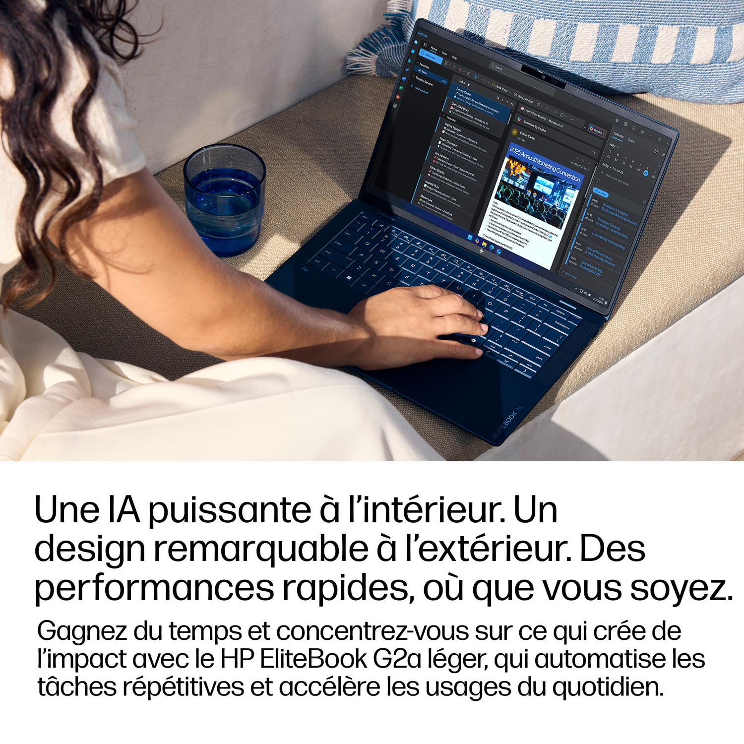 Une personne tape sur un HP EliteBook bleu avec un verre d'eau à proximité.