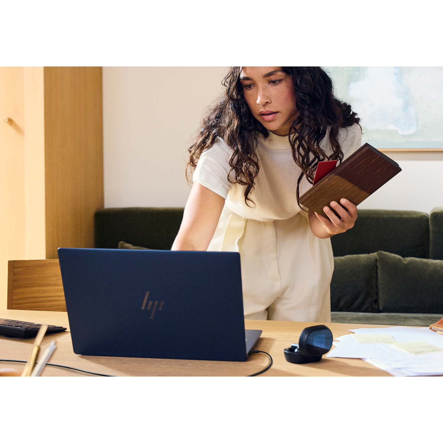 Vrouw met donker krullend haar houdt houten samples vast bij een laptop op een bureau.