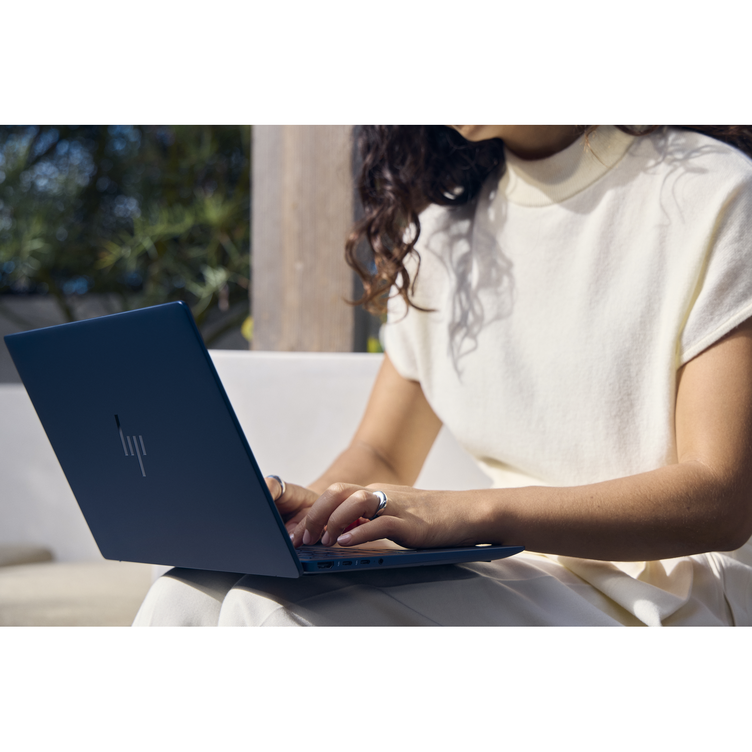 Een vrouw typt op een blauwe laptop, buiten zittend.