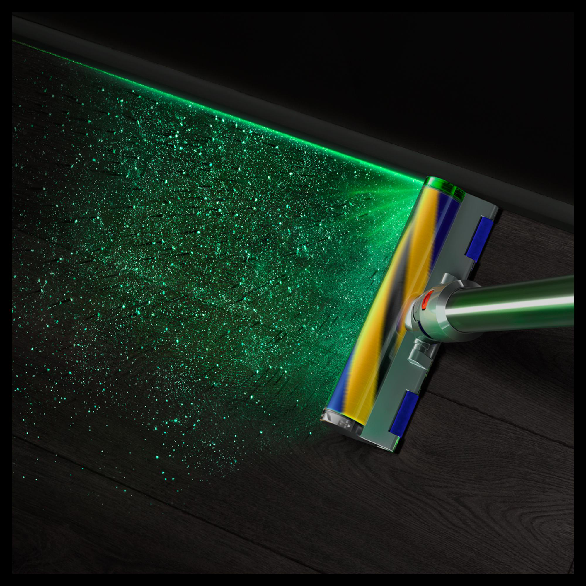 Ein Staubsaugerkopf mit grünem Licht beleuchtet Staubpartikel auf einem dunklen Holzboden.