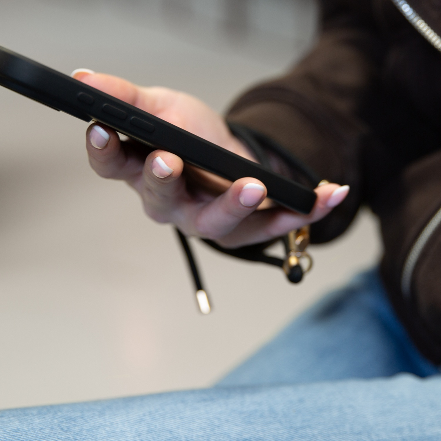 A hand with a manicure holds a black smartphone. A strap is attached.