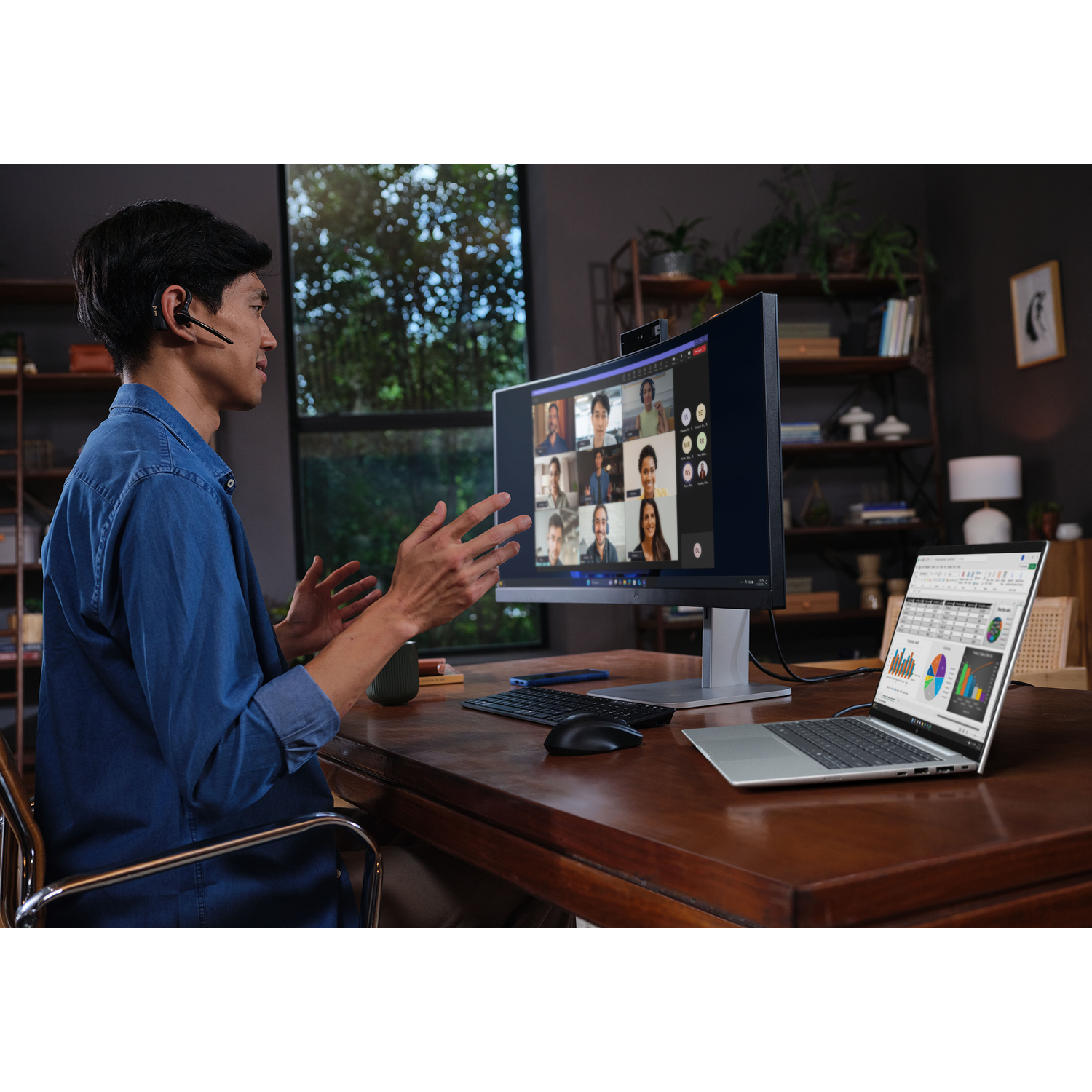 Man in blauw shirt in videogesprek, laptop met grafieken open op bureau.