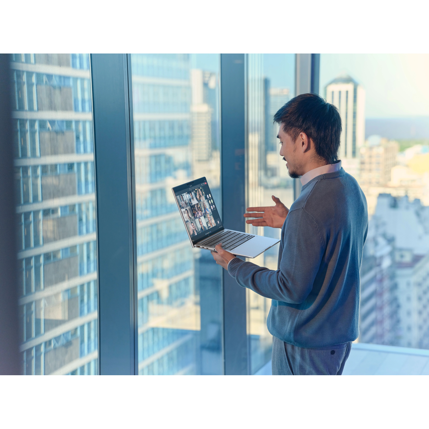Man in videogesprek met meerdere mensen op laptopscherm, stadszicht.