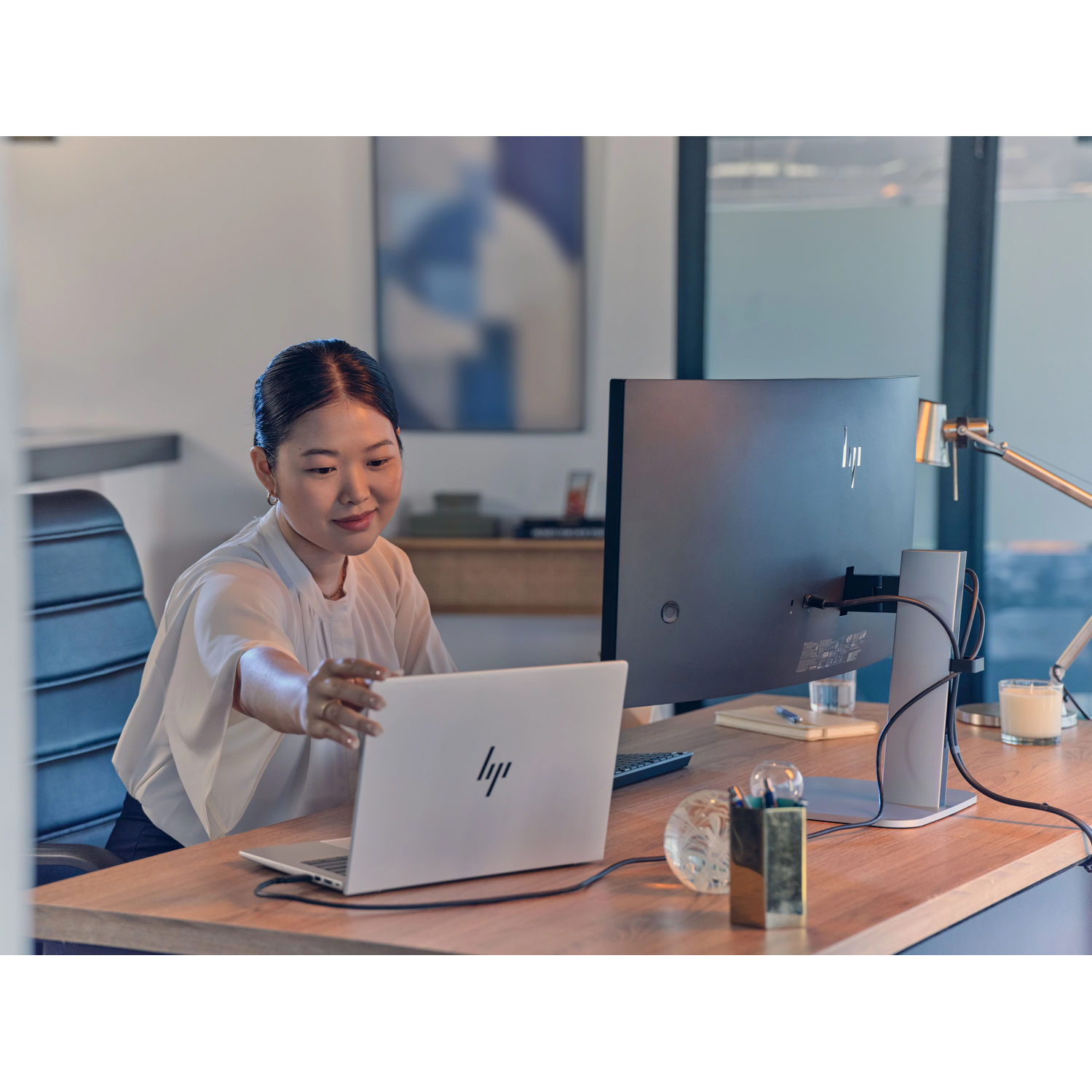 Een vrouw in een wit shirt zit aan een bureau en werkt op een laptop.