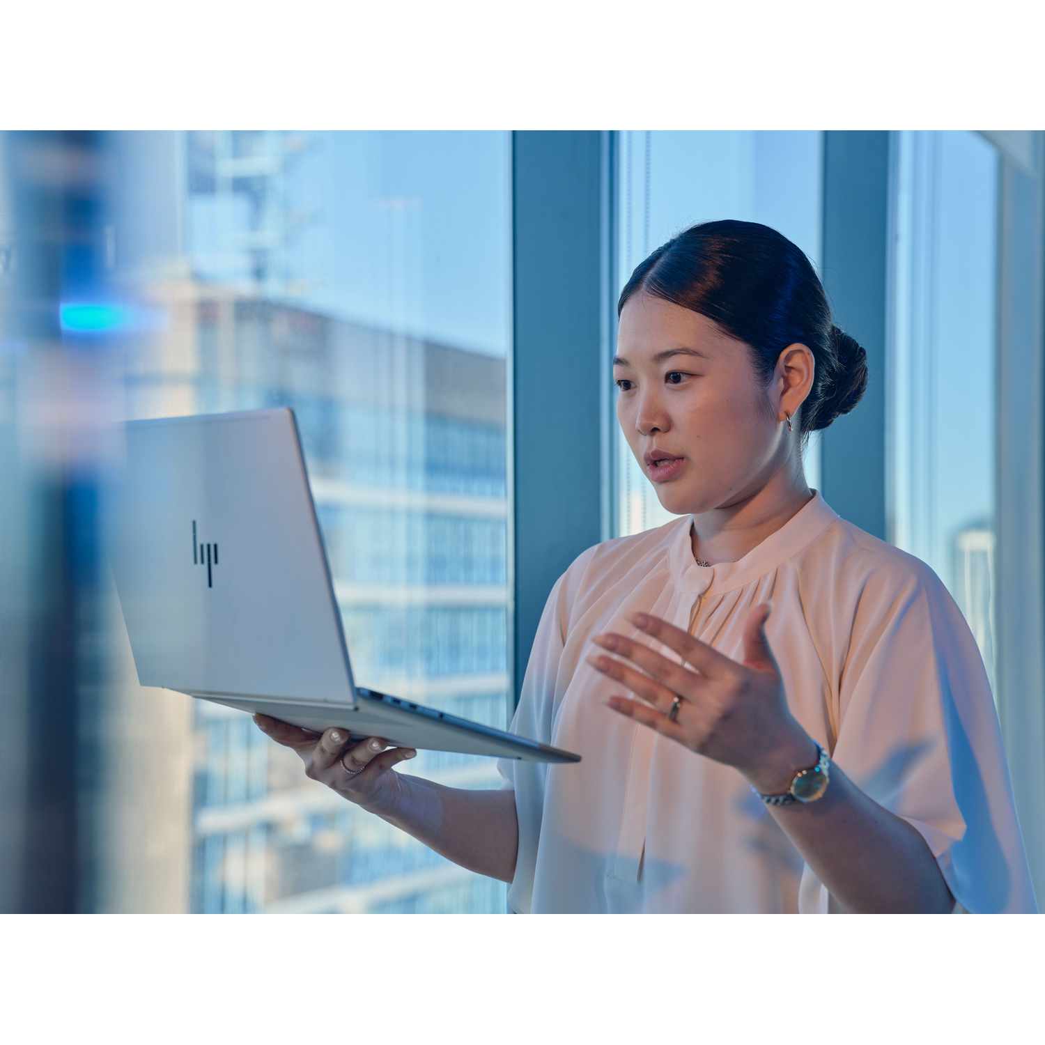 Een vrouw houdt een laptop vast voor een raam met uitzicht op een stad.