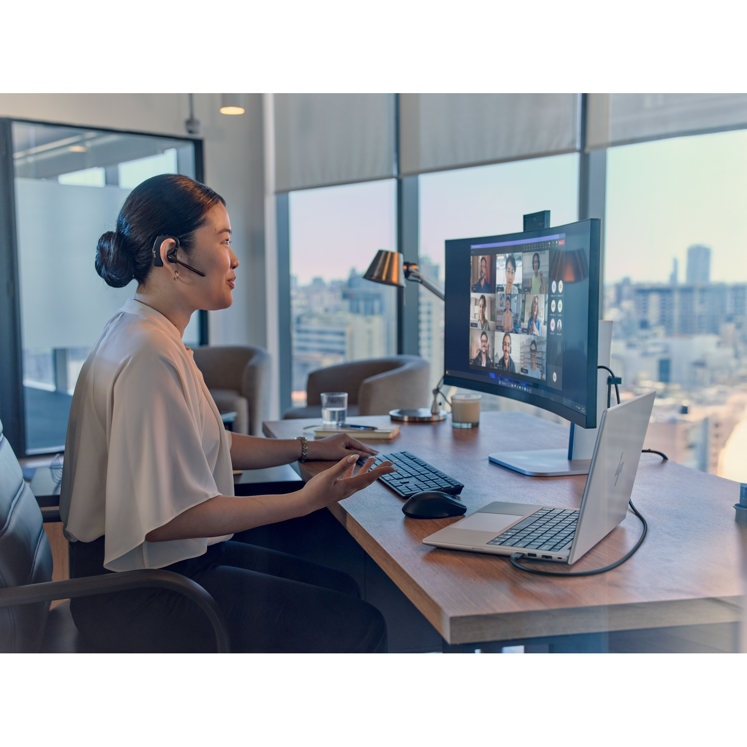 Vrouw met headset op kantoor in videogesprek op grote monitor.