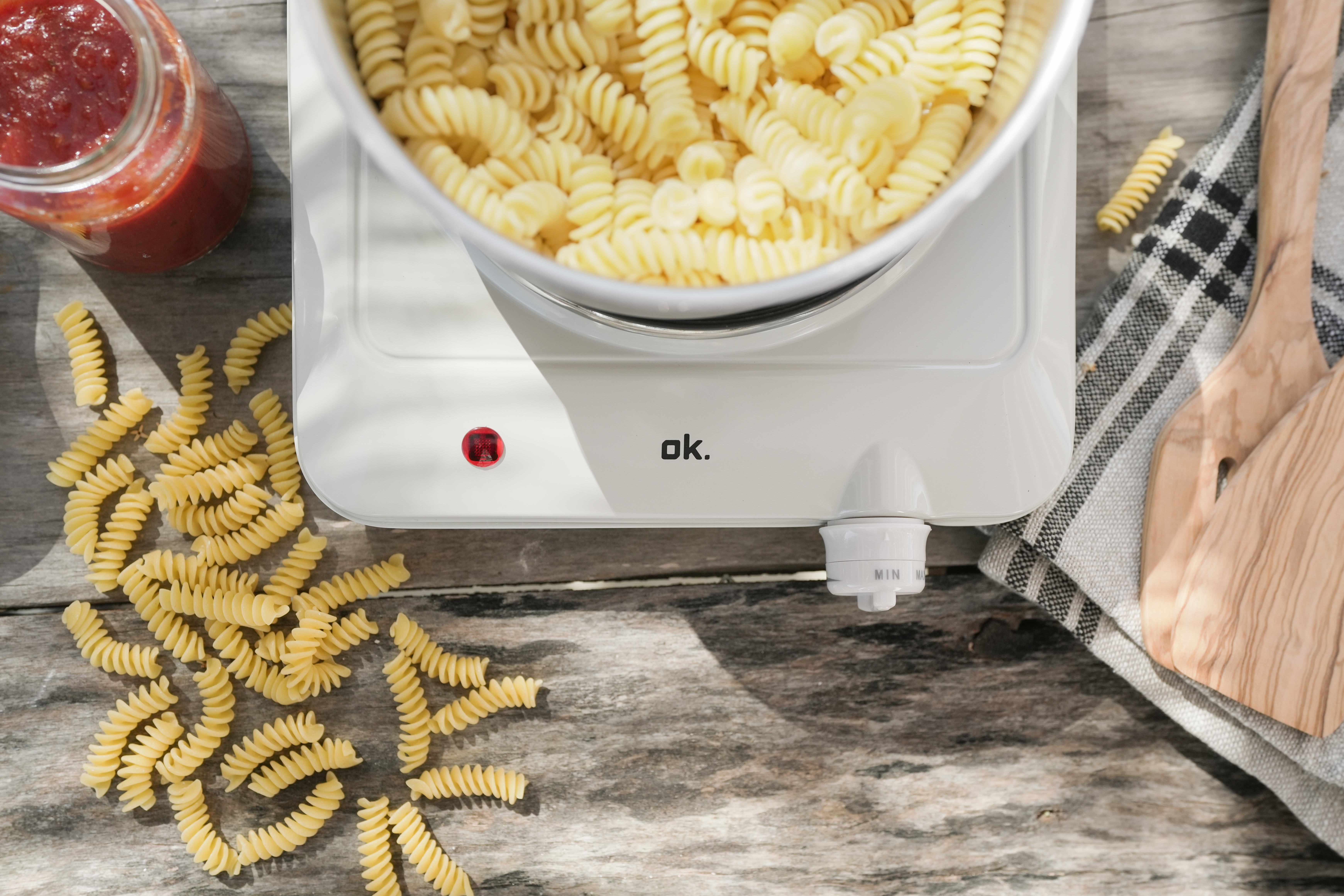 Un pot de sauce tomate, une casserole de pâtes fusilli et des cuillères en bois.