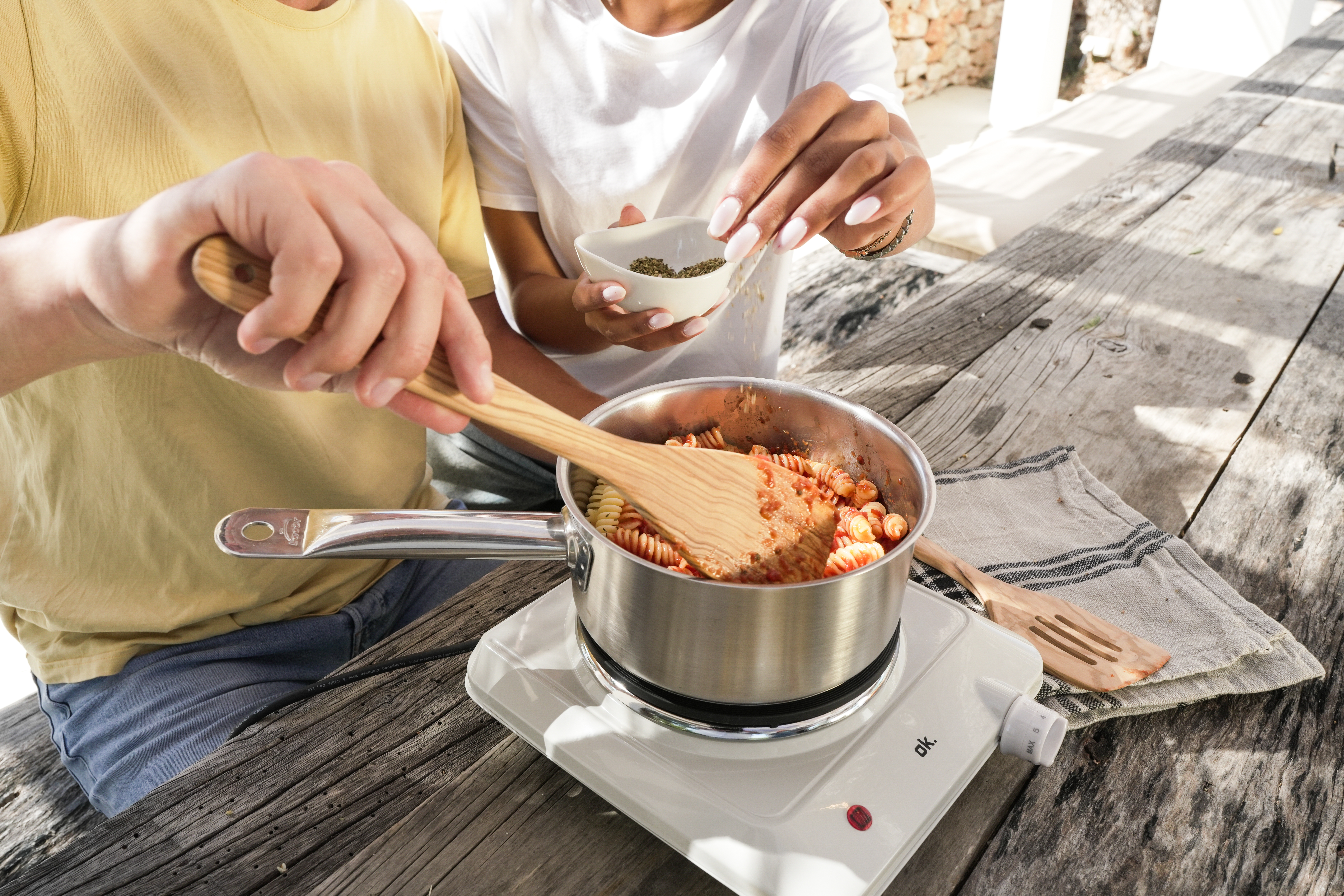 Deux personnes font cuire des pâtes avec de la sauce dans une casserole sur un réchaud.