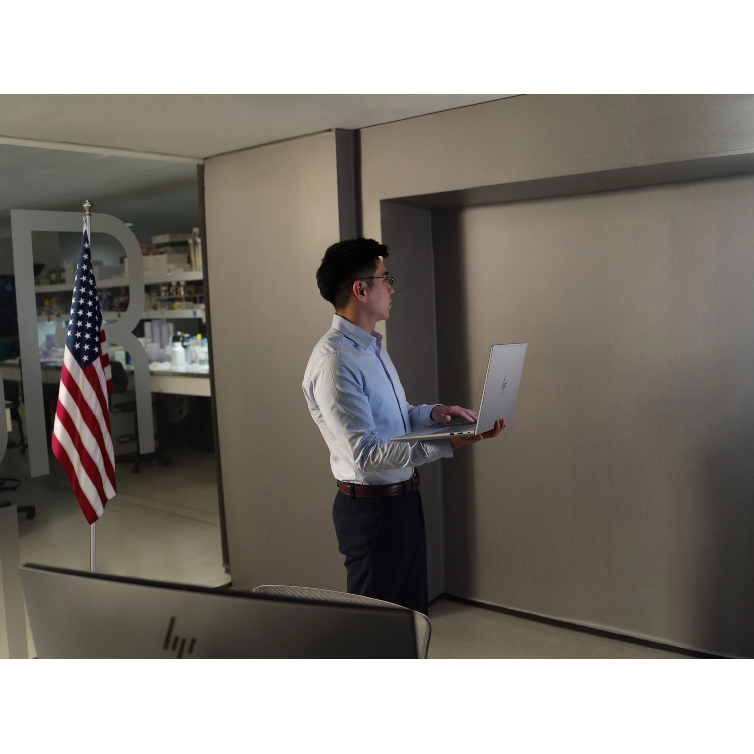 Een man met een bril houdt een laptop vast in een kantoor met een Amerikaanse vlag.