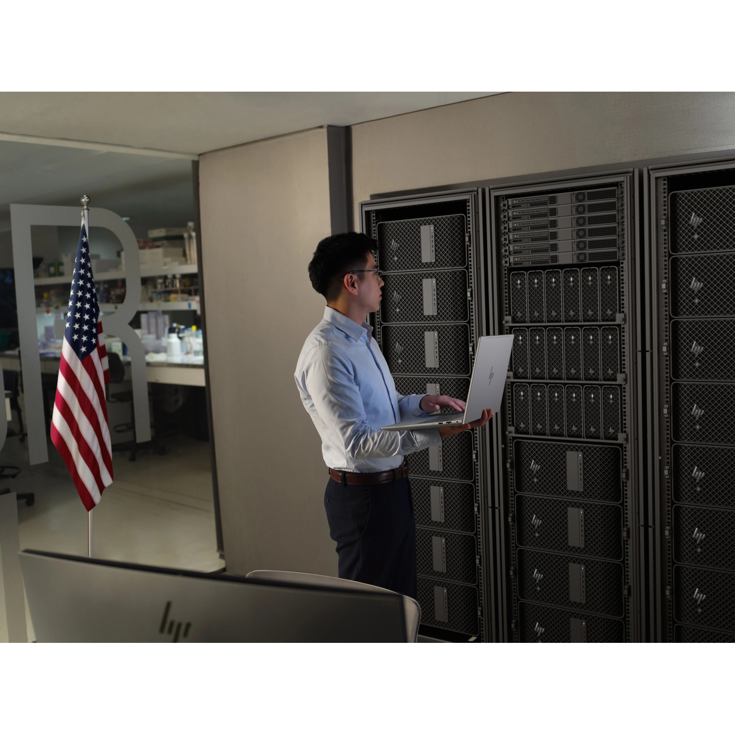 Een man met laptop staat voor serverracks. Een Amerikaanse vlag is zichtbaar.