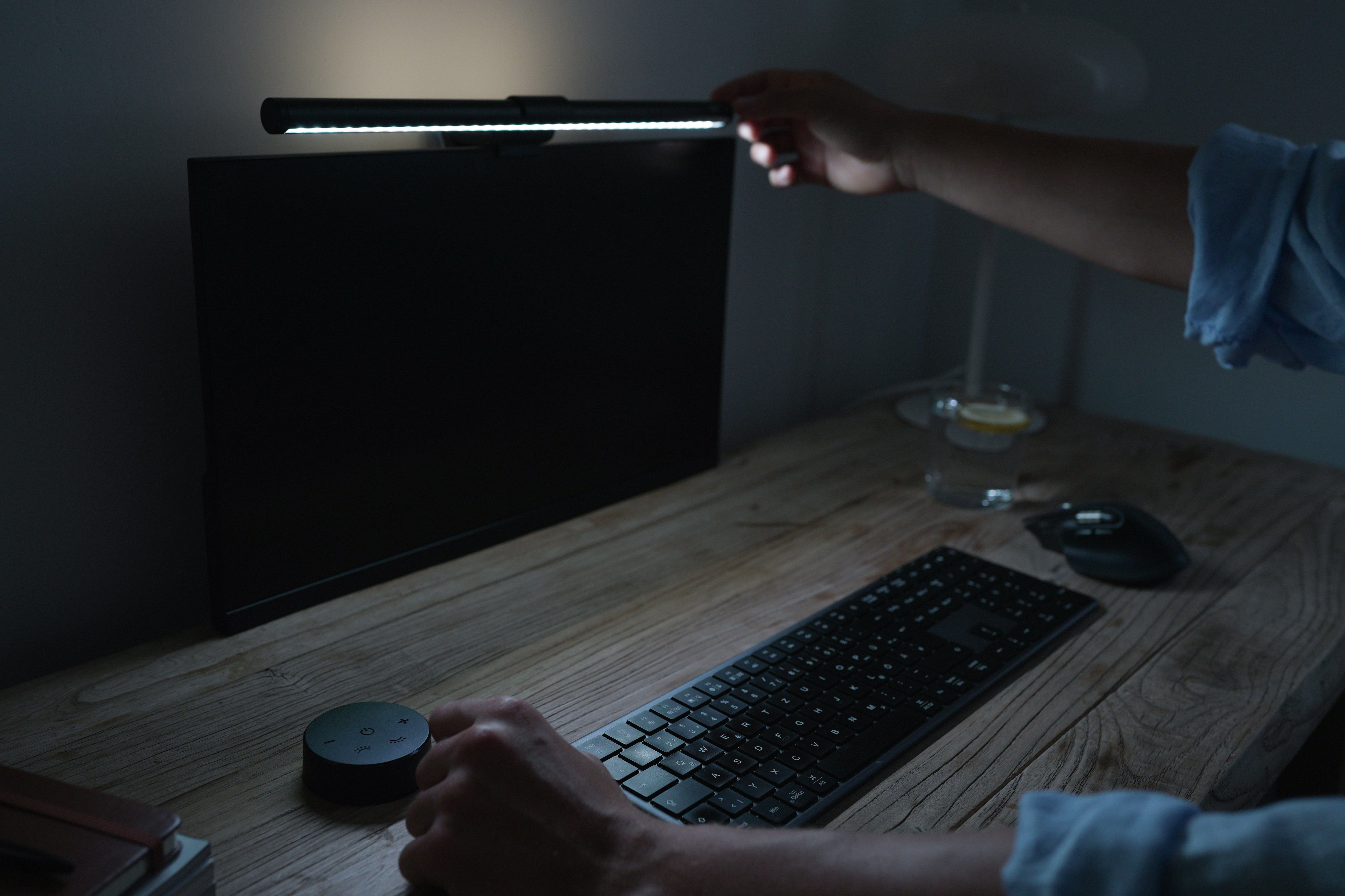Eine Hand passt eine Schreibtischlampe über einem dunklen Monitor an. Tastatur, Maus, Glas.