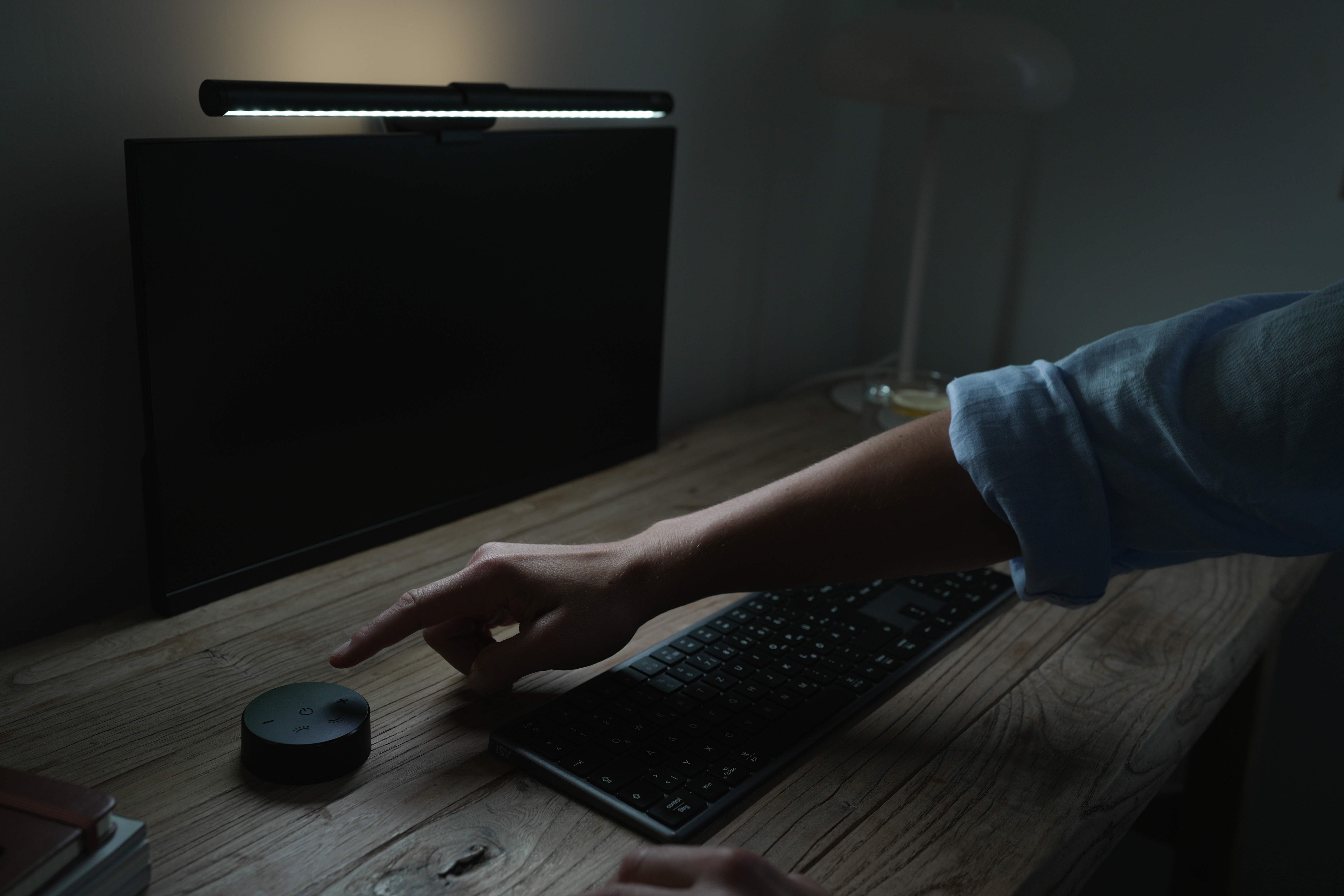 Eine Hand berührt einen runden schwarzen Knopf neben einer Tastatur und einem Monitor.
