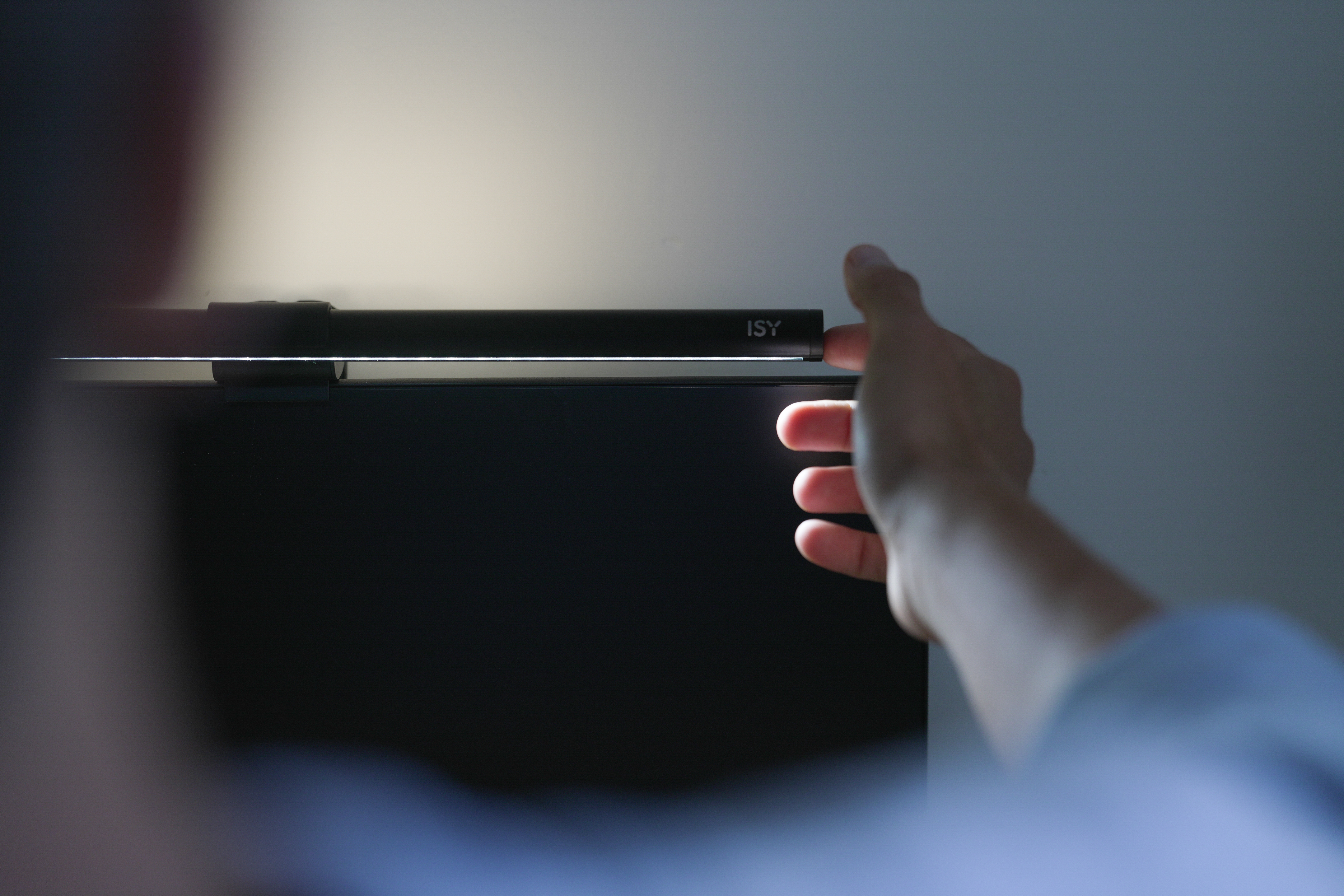 Eine Hand stellt eine schwarze ISY-Lichtleiste auf einem Computermonitor ein.