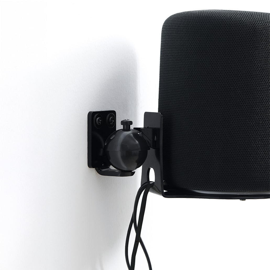 Support d'enceinte noir avec rotule sur mur blanc, câbles pendant.