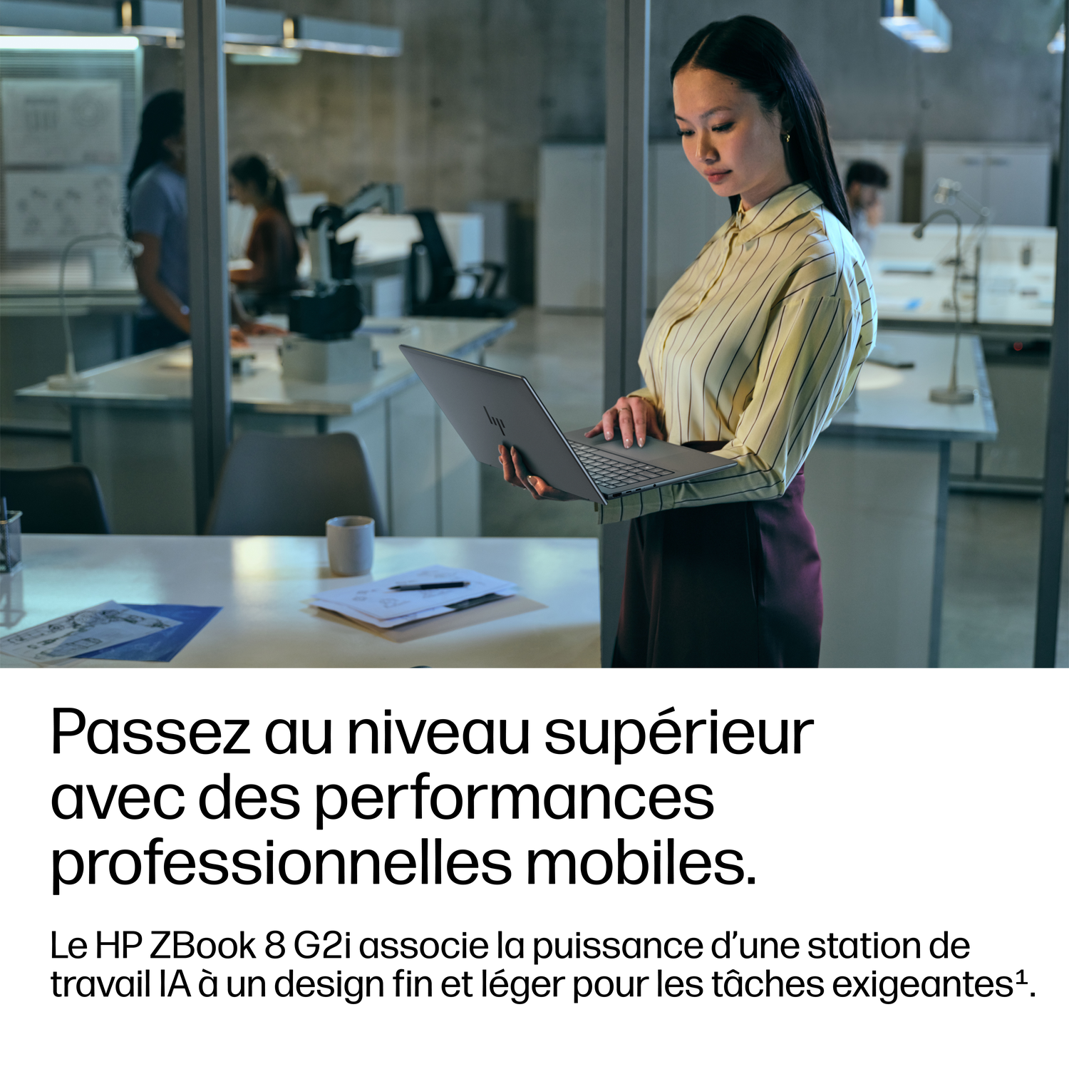 Une femme tenant un ordinateur portable dans un bureau moderne, des collègues travaillent en arrière-plan.