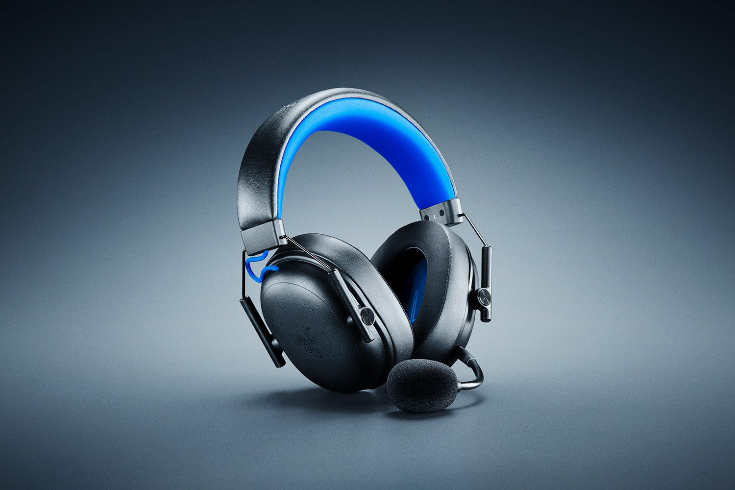 Auriculares negros para juegos con detalles azules y micrófono sobre fondo gris.