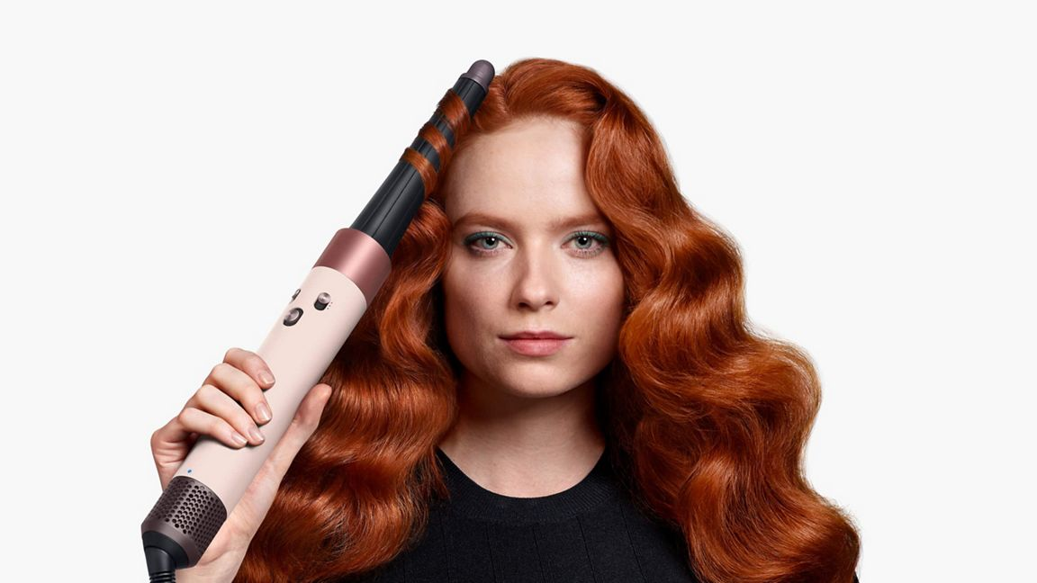 Donna con capelli rossi che usa un arricciacapelli, modellando una ciocca.