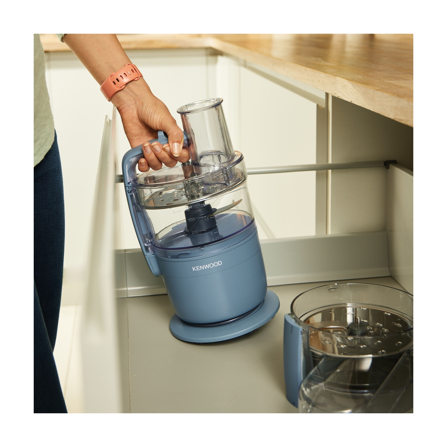 Una mano tiene un robot da cucina Kenwood blu con ciotola trasparente.