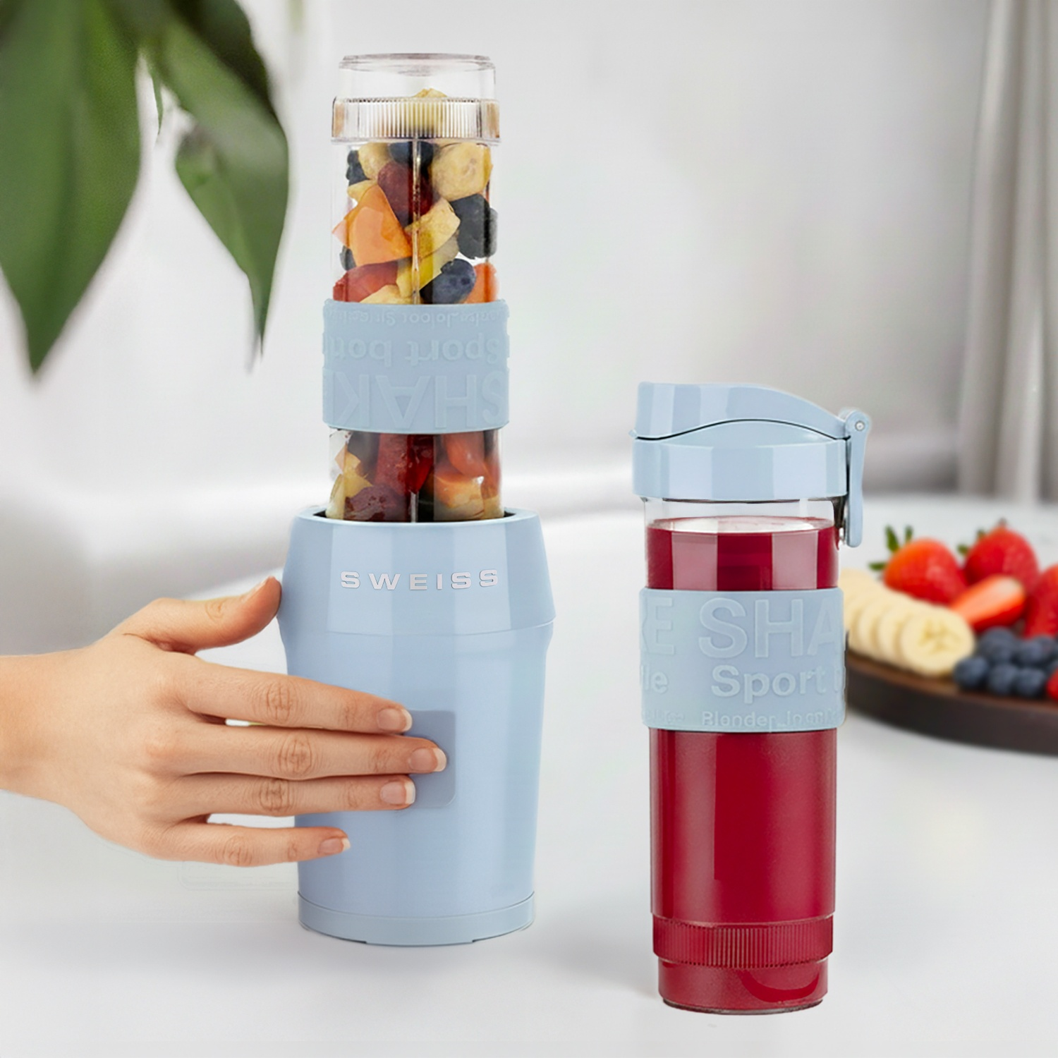 Un frullatore azzurro con frutta e accanto una tazza di succo rosso.