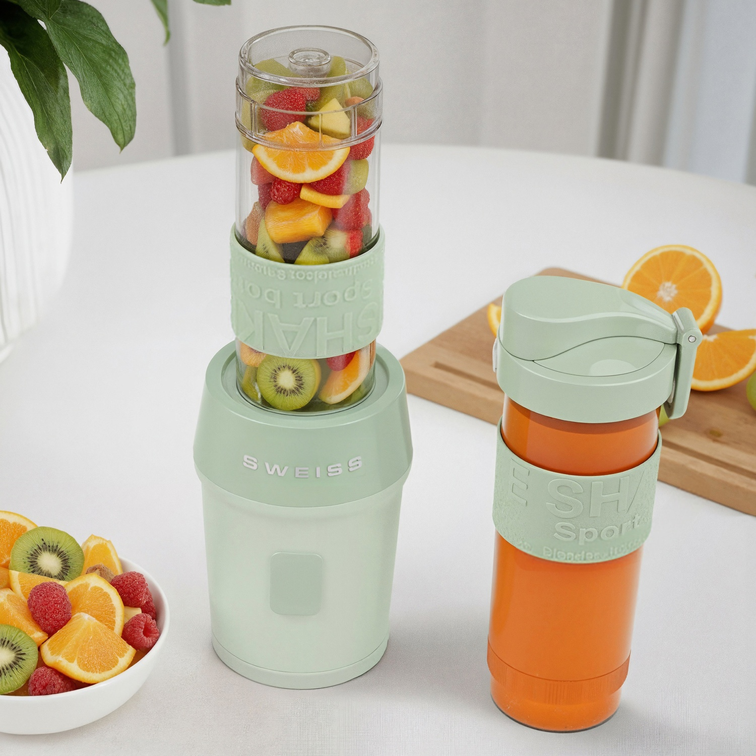 Un frullatore verde con frutta accanto a una tazza da viaggio arancione.