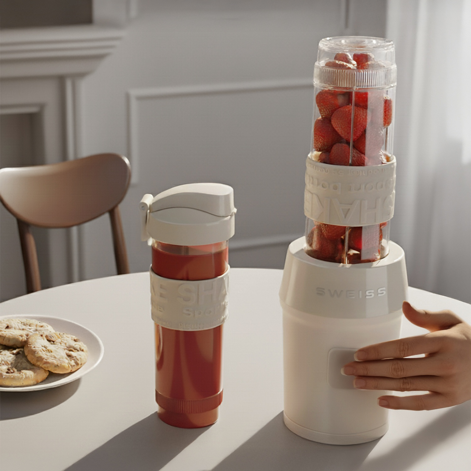 Un frullatore portatile con fragole e una tazza di succo sono su un tavolo con biscotti.