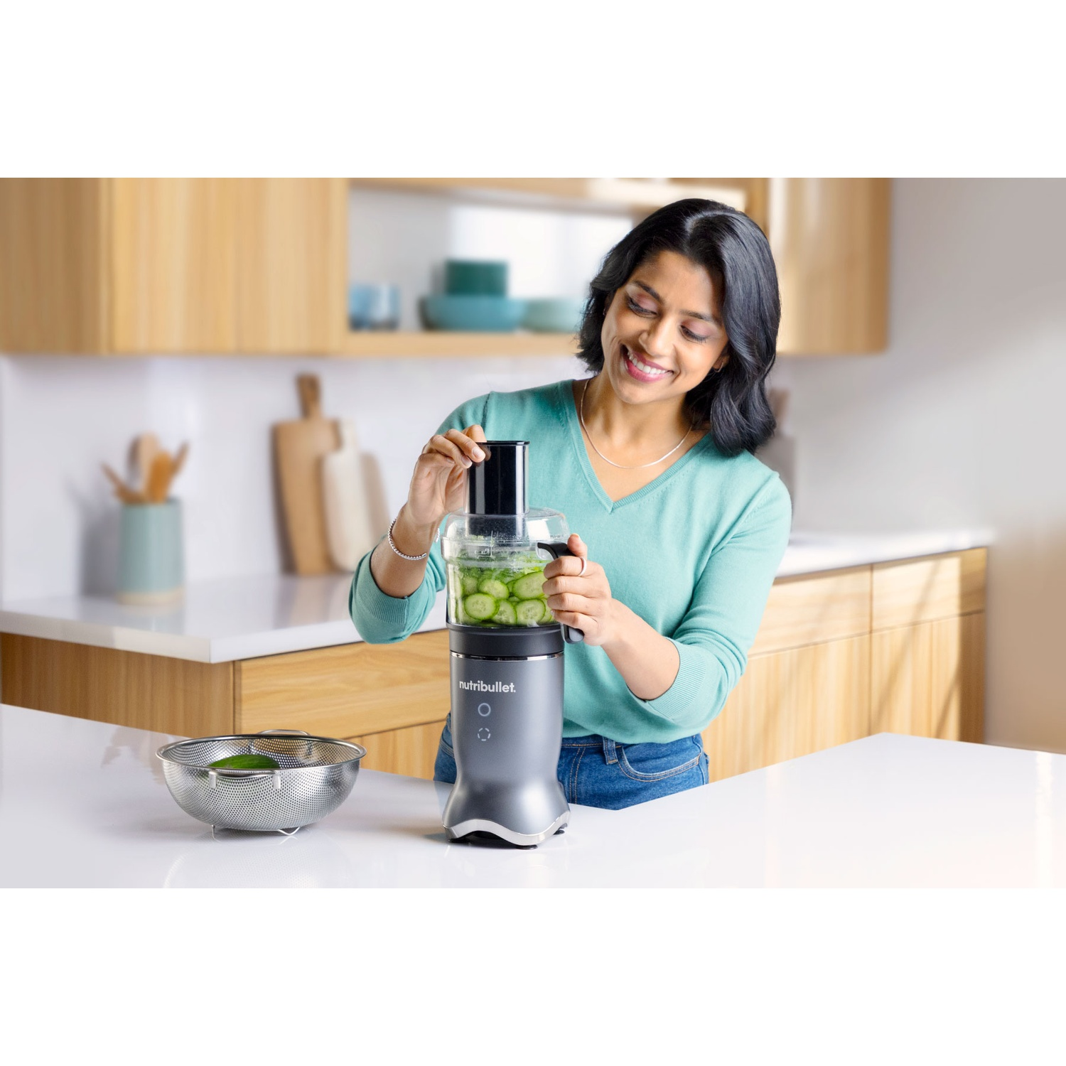 Una donna usa un robot da cucina Nutribullet con fette di cetriolo.