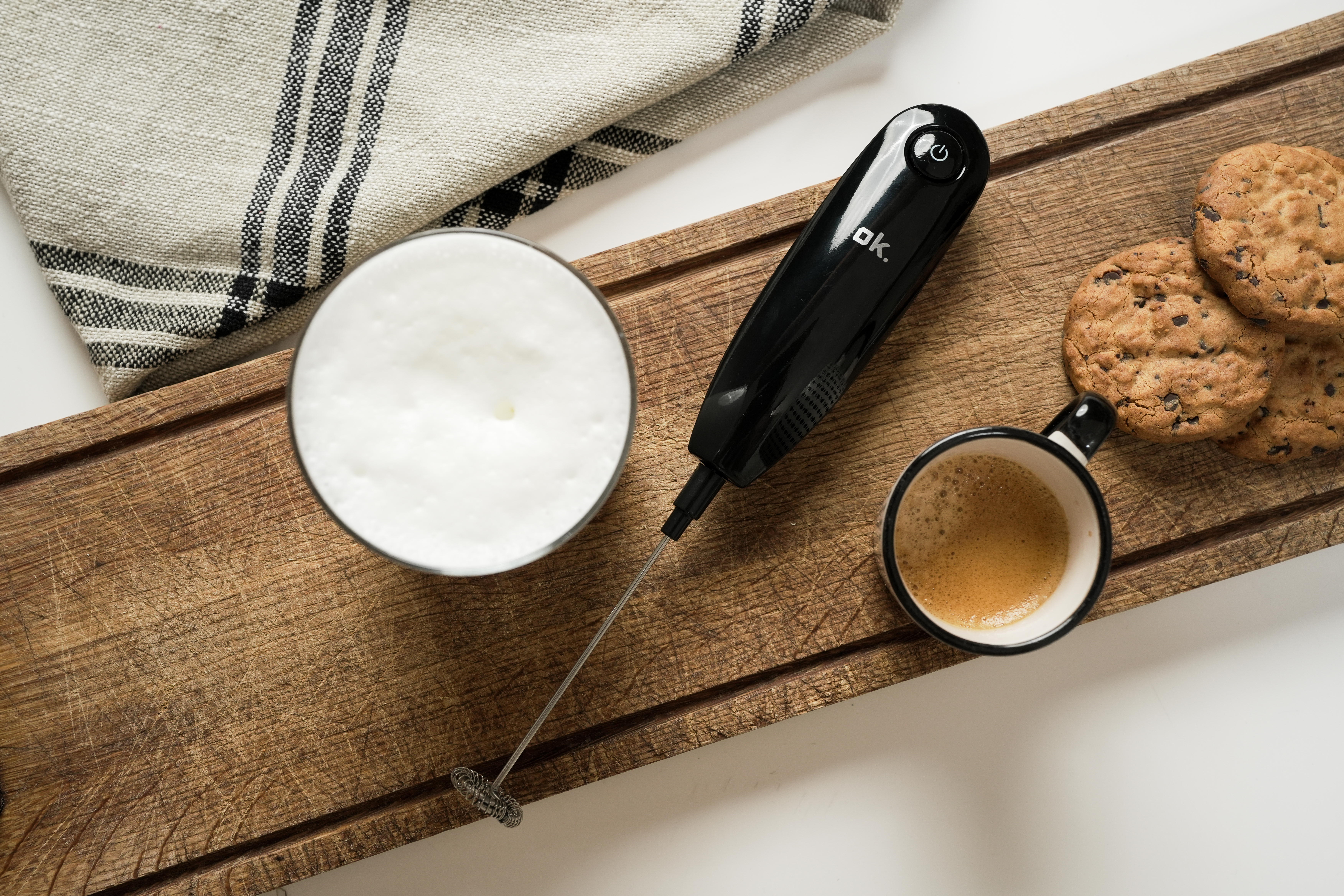 Un mousseur à lait repose à côté de tasses de café et de biscuits sur une planche en bois.