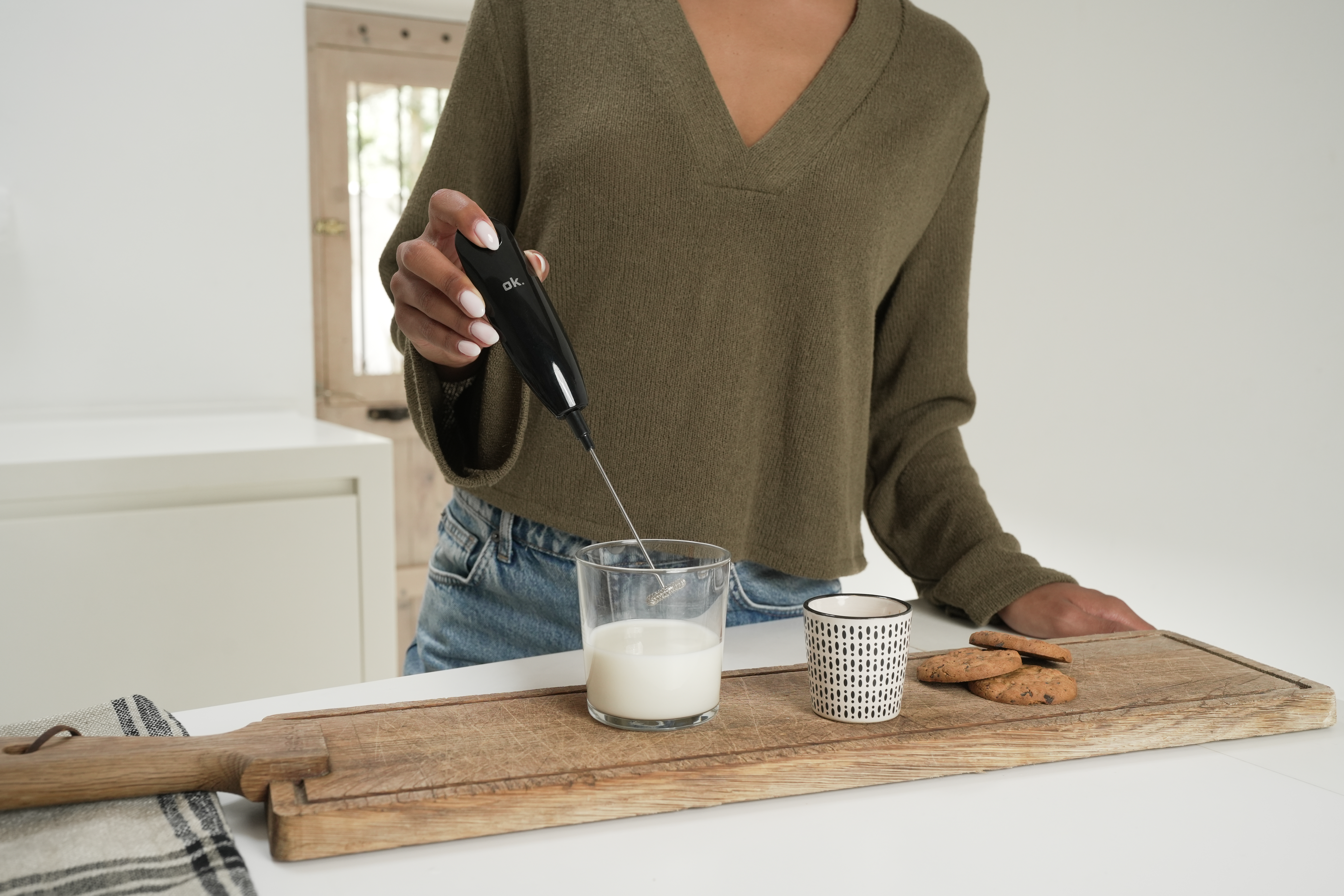 Une personne fait mousser du lait dans un verre avec un mousseur à main sur une table.