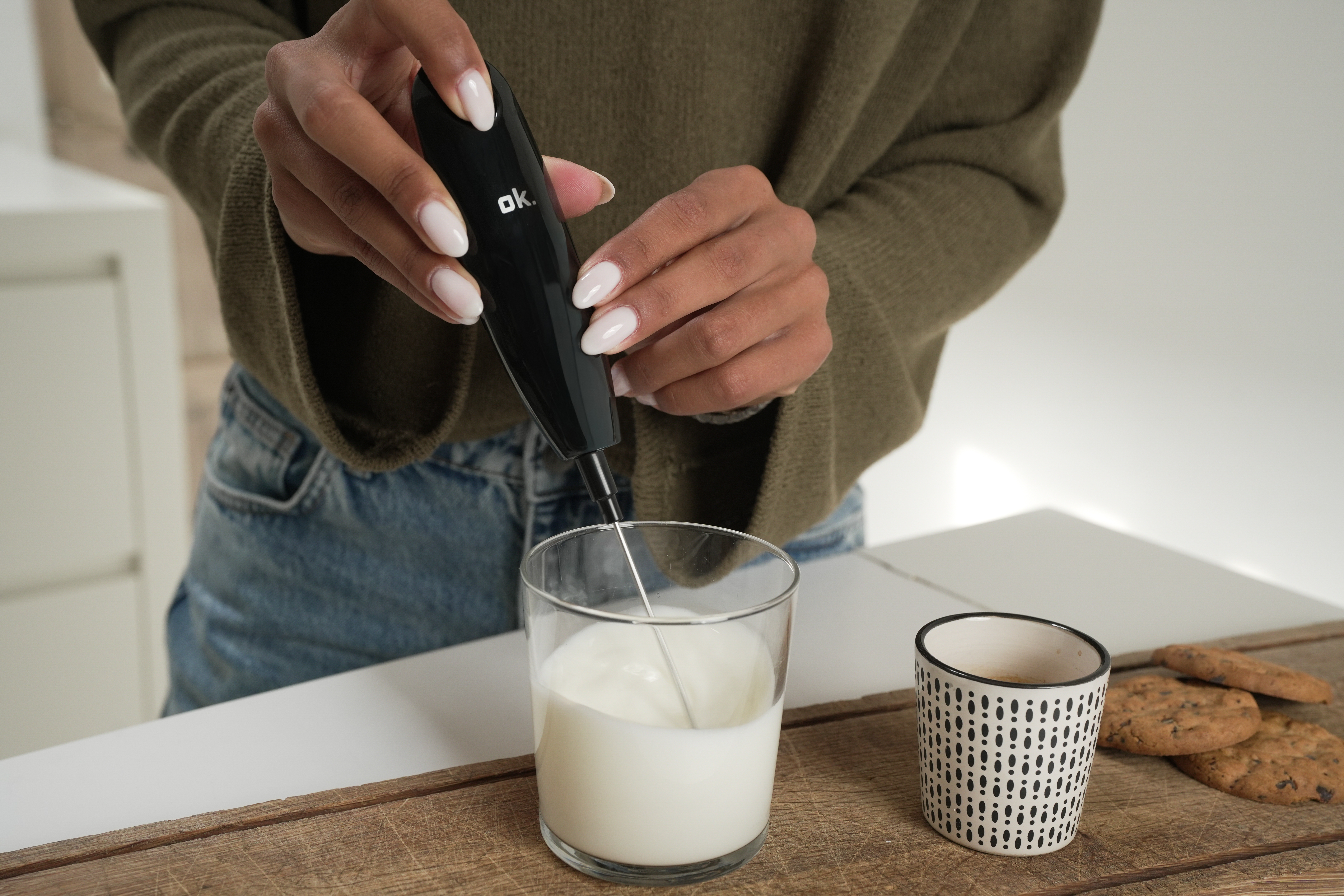 Une personne fait mousser du lait dans un verre avec un mousseur à lait noir.