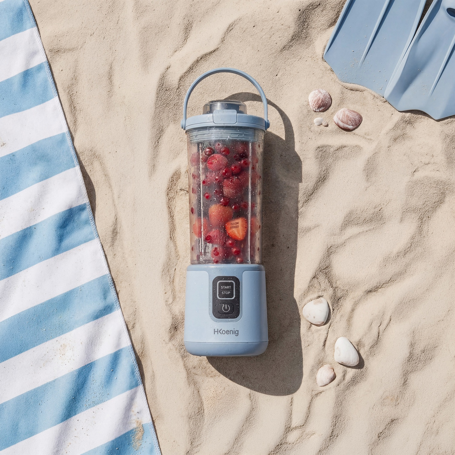 Un frullatore portatile con frutta sulla sabbia, vicino a conchiglie e pinne.