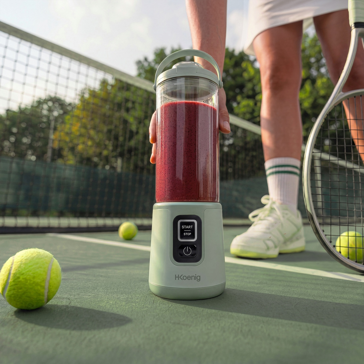 Un frullatore pieno di bacche si trova su un campo da tennis. Si vedono palline e racchette da tennis.