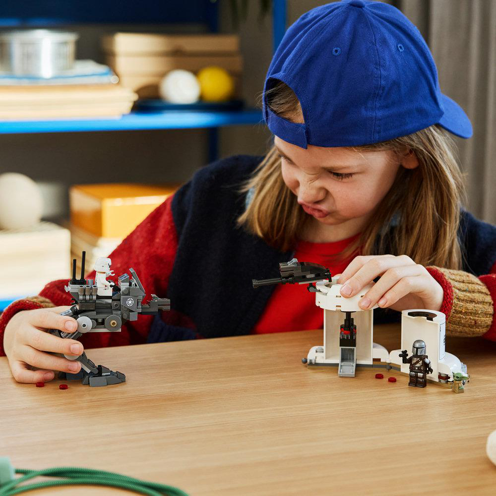 Ein Mädchen mit blauer Kappe spielt mit Lego Star Wars Sets auf Holztisch.