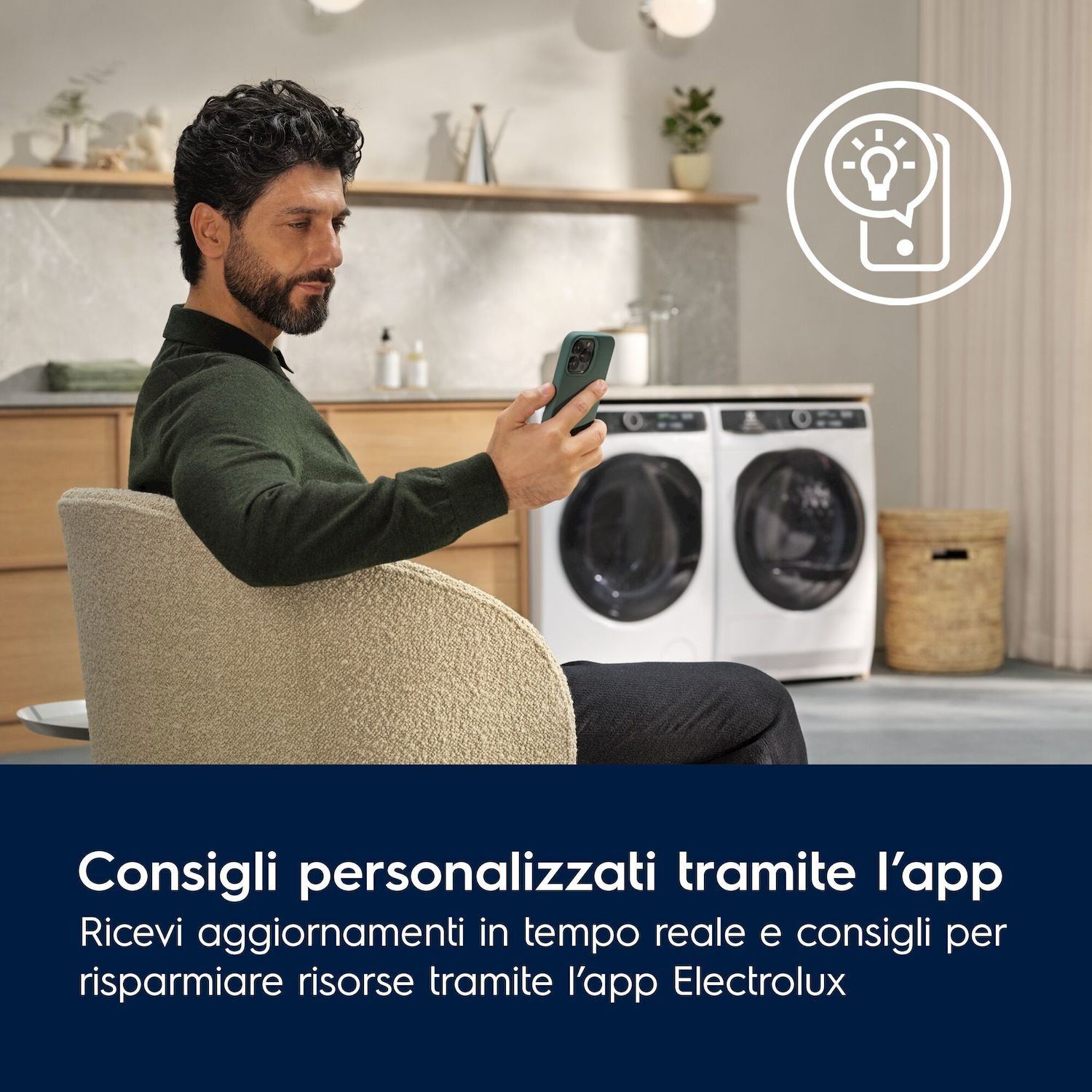 Uomo seduto su sedia, tiene telefono. Lavatrici sullo sfondo.