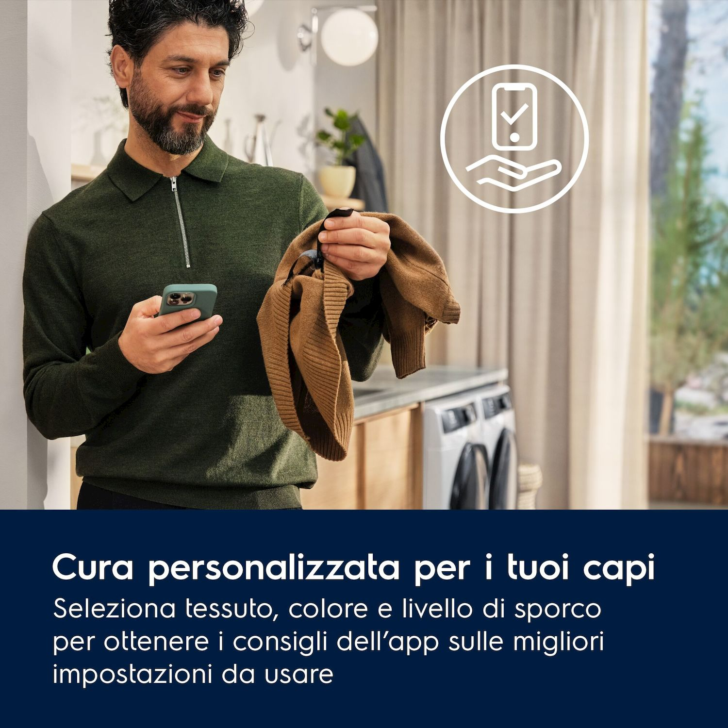 Uomo con smartphone e maglione marrone davanti lavatrice.