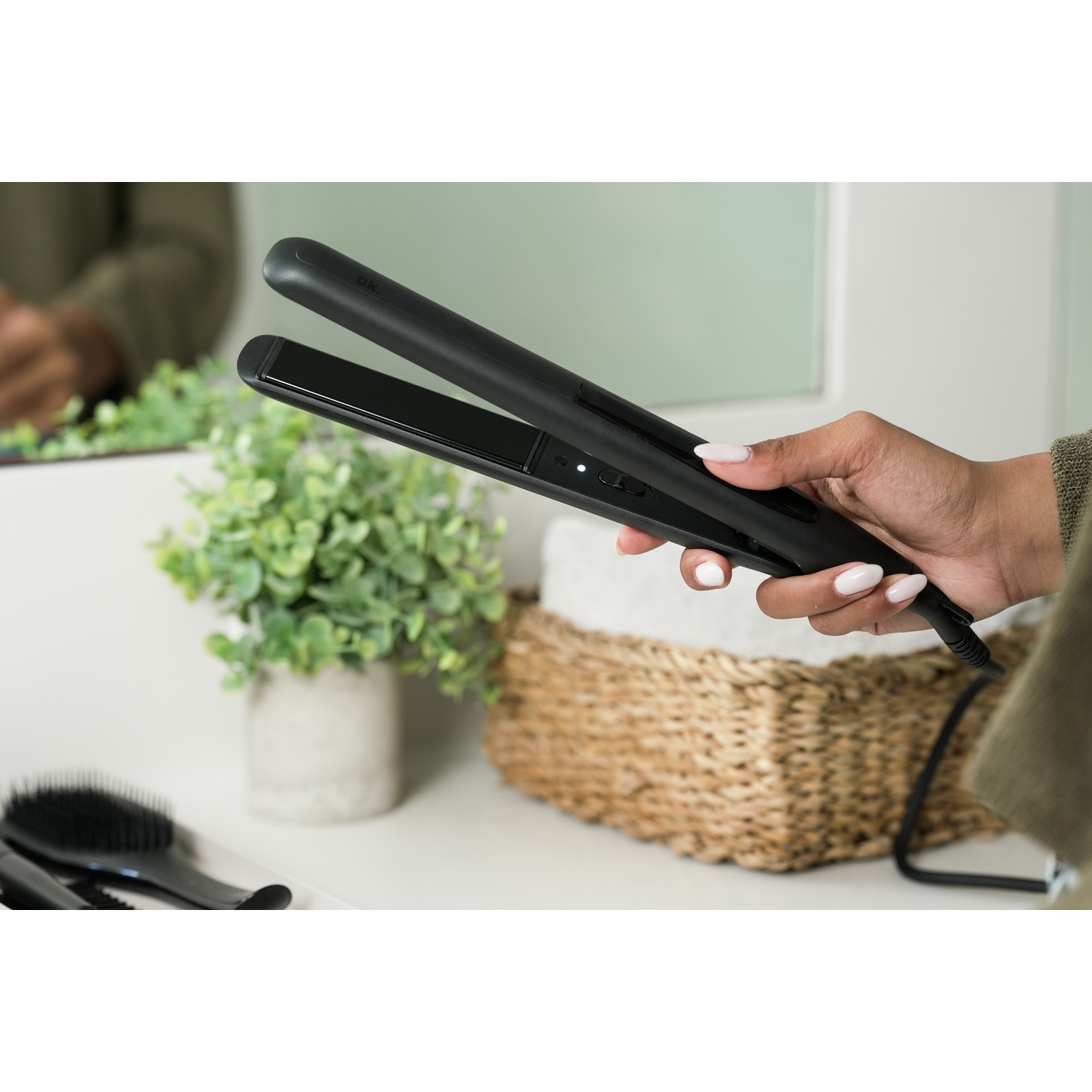 Una mano tiene una piastra nera su un mobile da bagno con piante.
