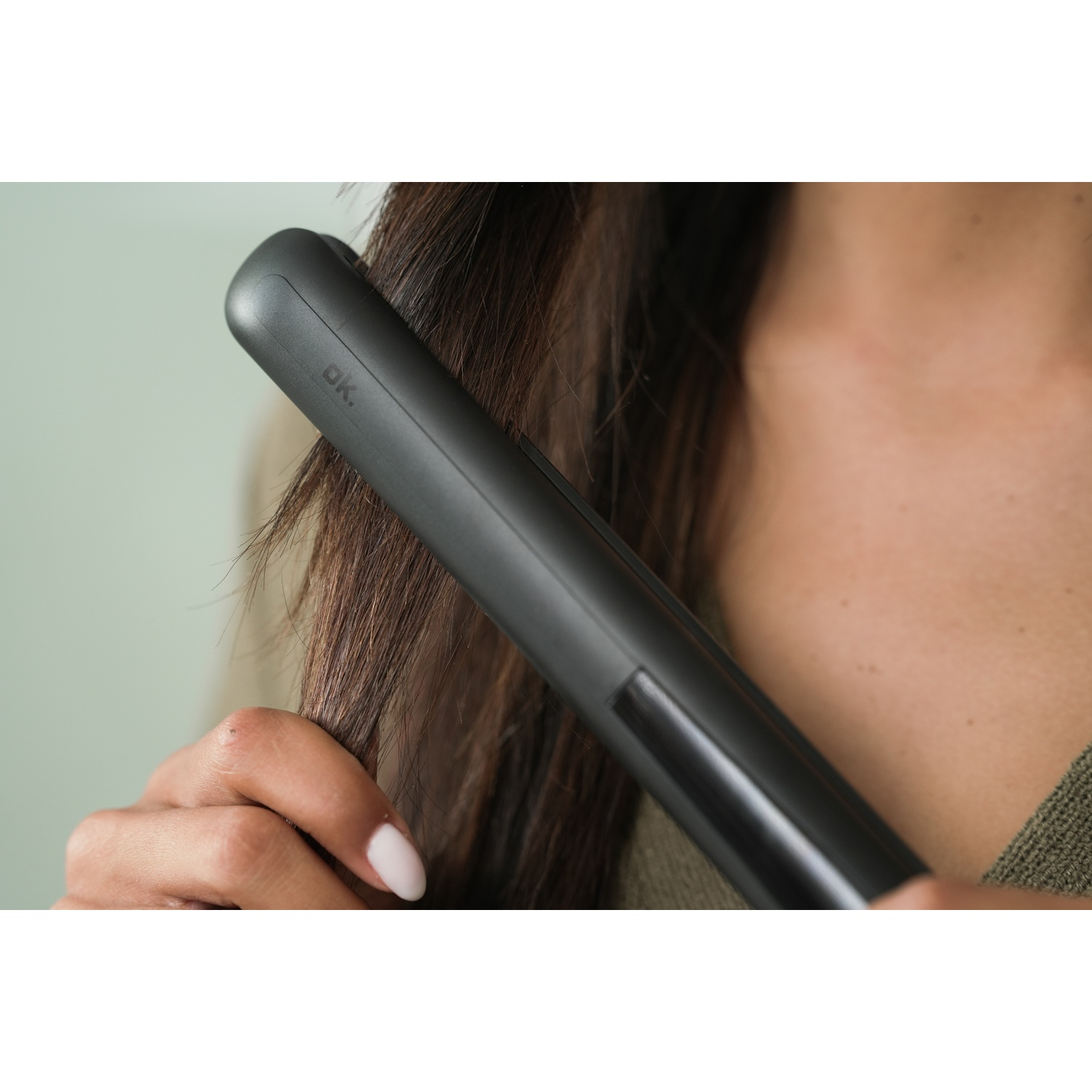 Una persona si sta lisciando i capelli castani con una piastra nera.