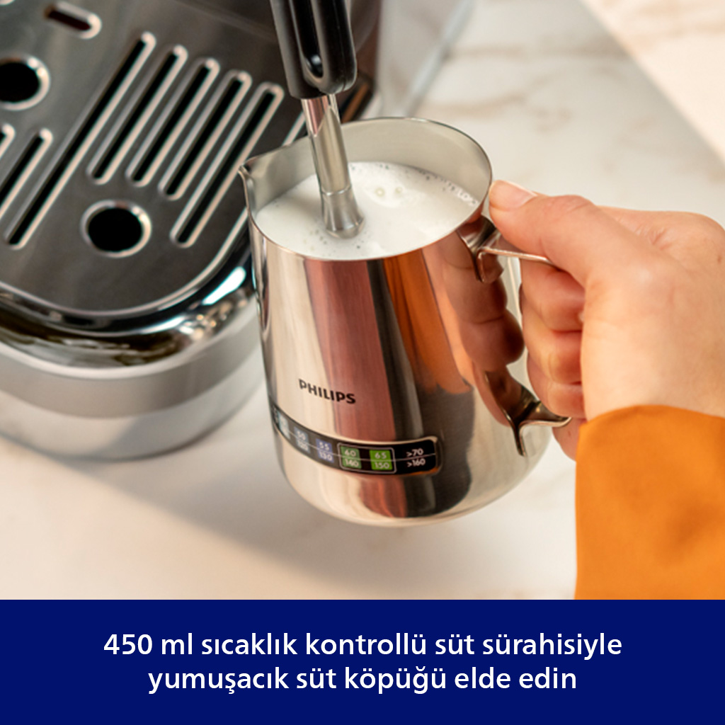 Bir el, kahve makinesinin yanında sıcak sütlü süt köpürtme sürahisi tutuyor.
