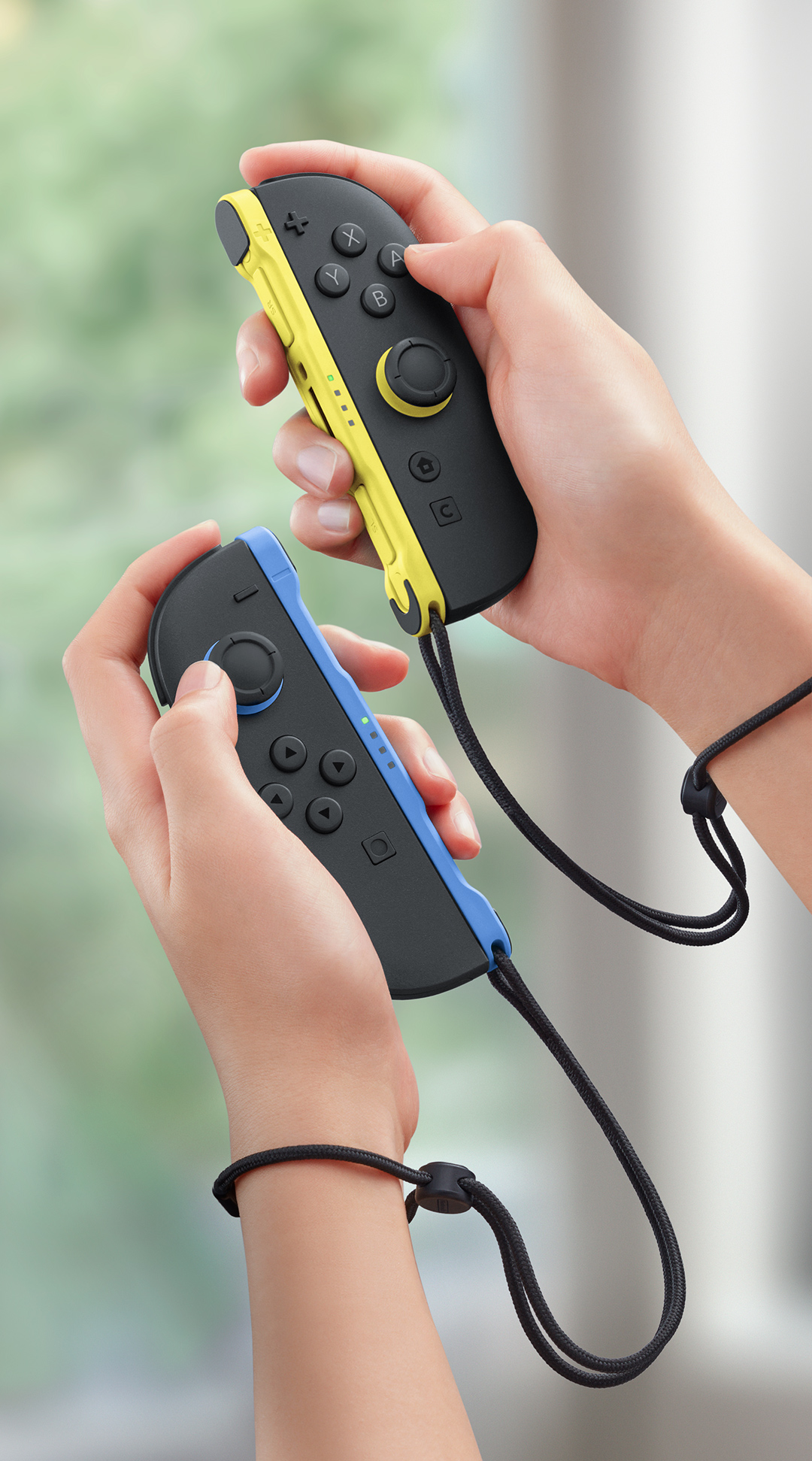 Bilek kayışlı sarı ve mavi Joy-Con kontrolcüler tutan eller.
