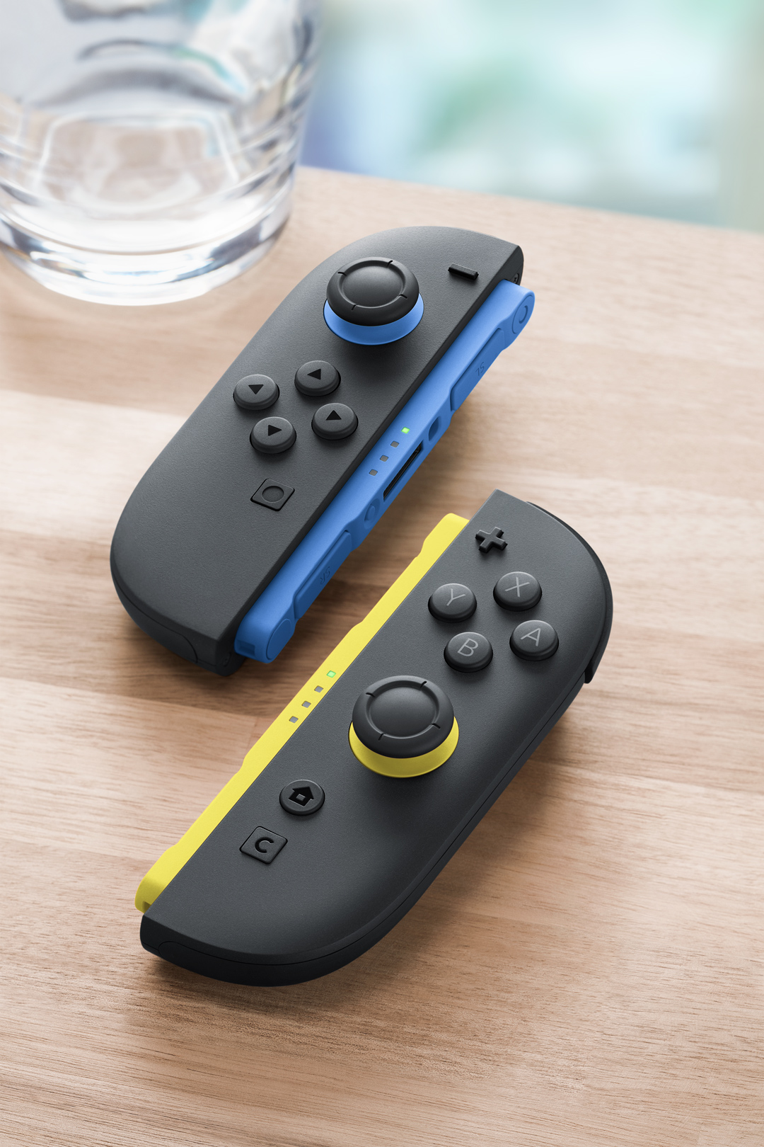 Mavi ve sarı vurgulara sahip iki siyah Joy-Con kumandası ahşap masada duruyor.