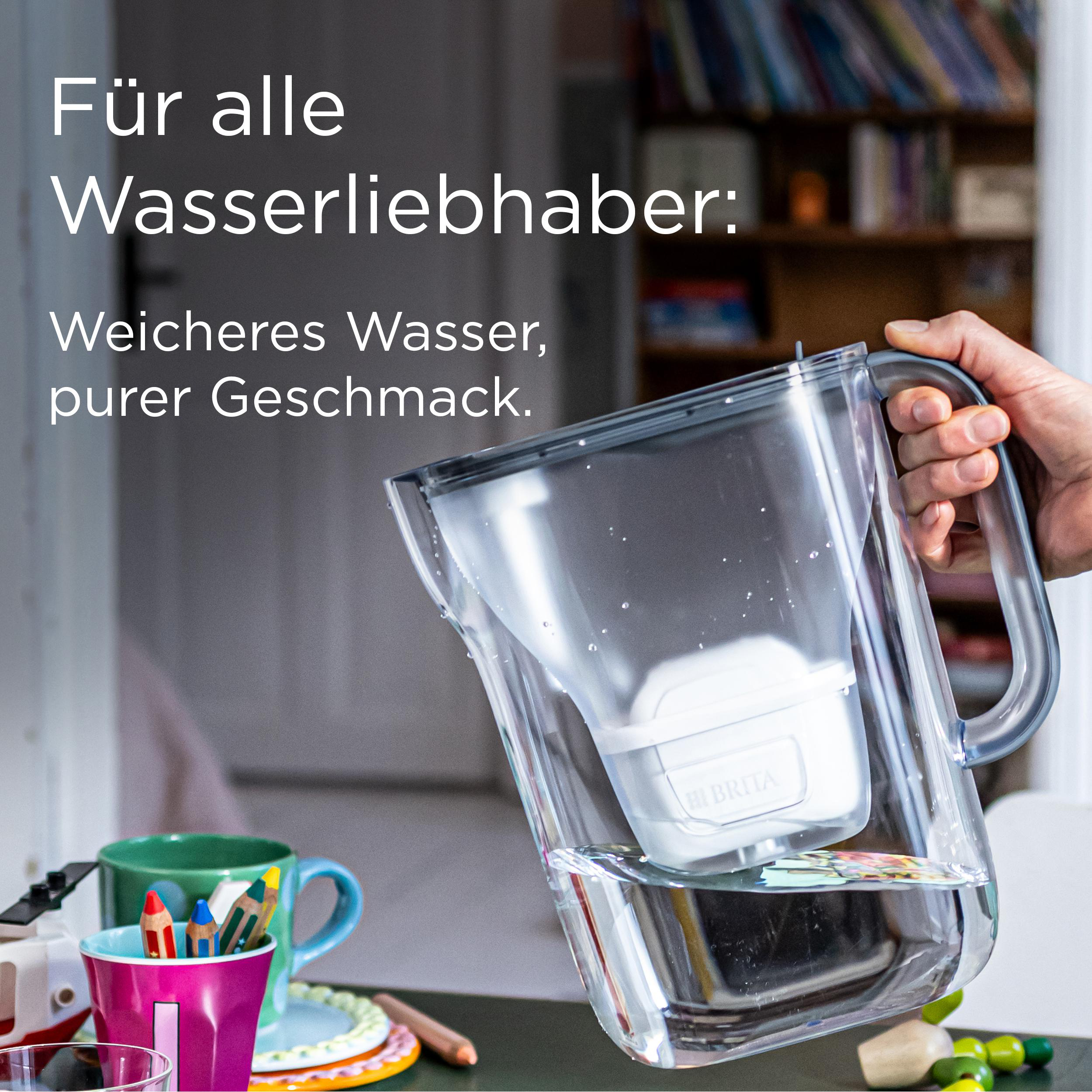Eine Hand hält eine Wasserfilterkanne. Buntstifte in einer Tasse im Vordergrund.