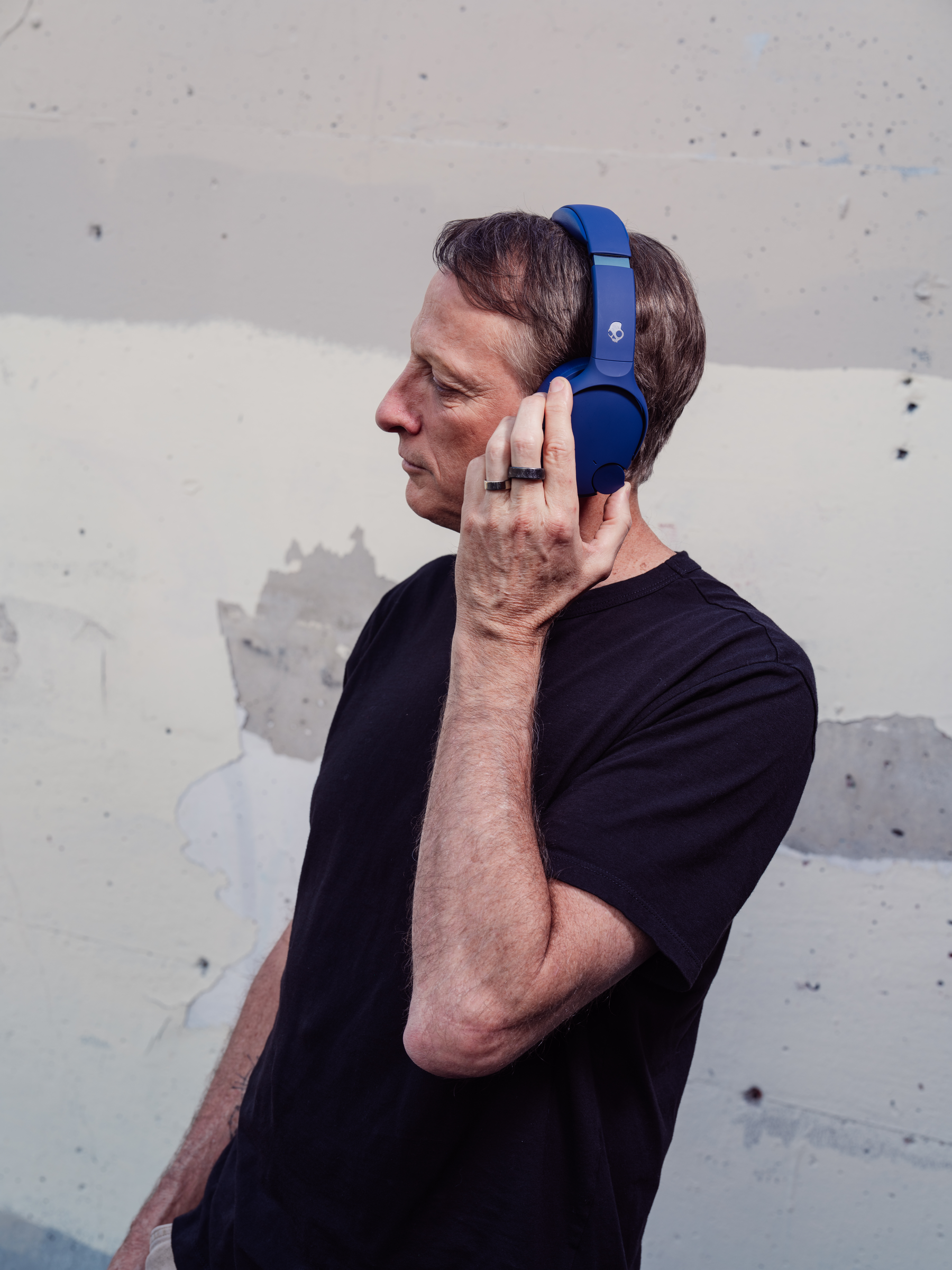Ein Mann mit blauen Kopfhörern im Profil, vor einer Wand stehend.