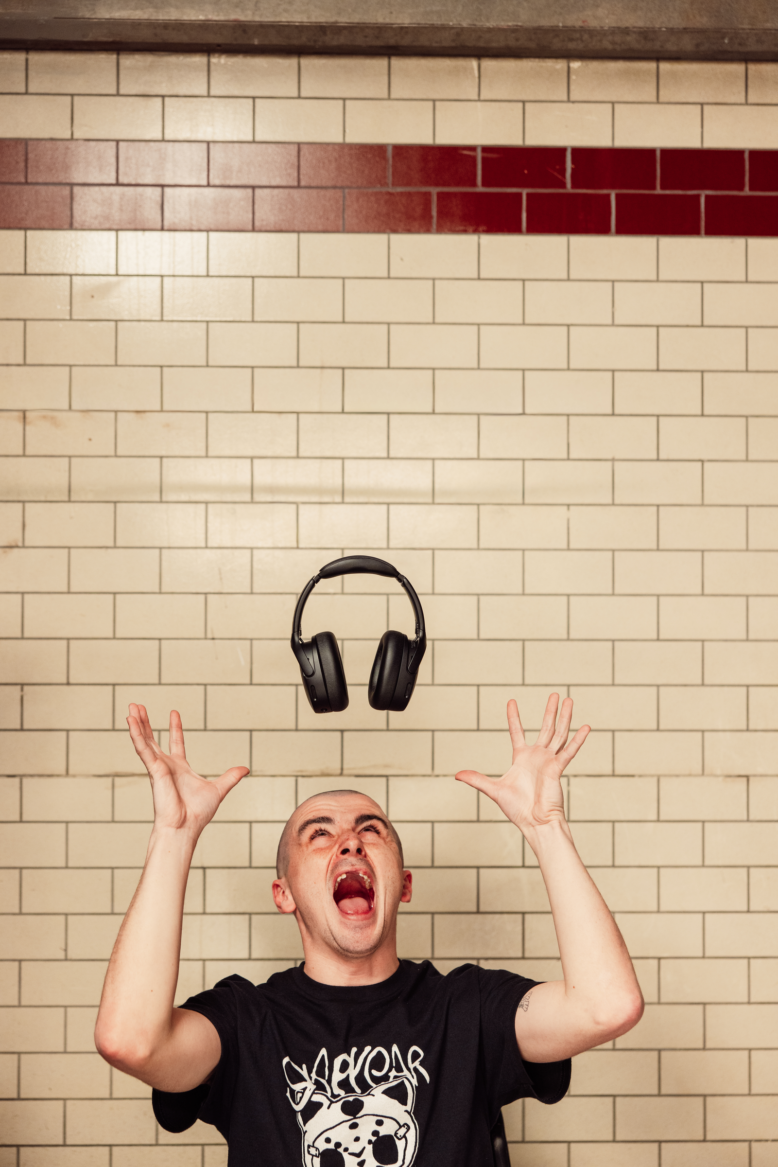 Ein Mann wirft Kopfhörer in die Luft vor einer gefliesten Wand.