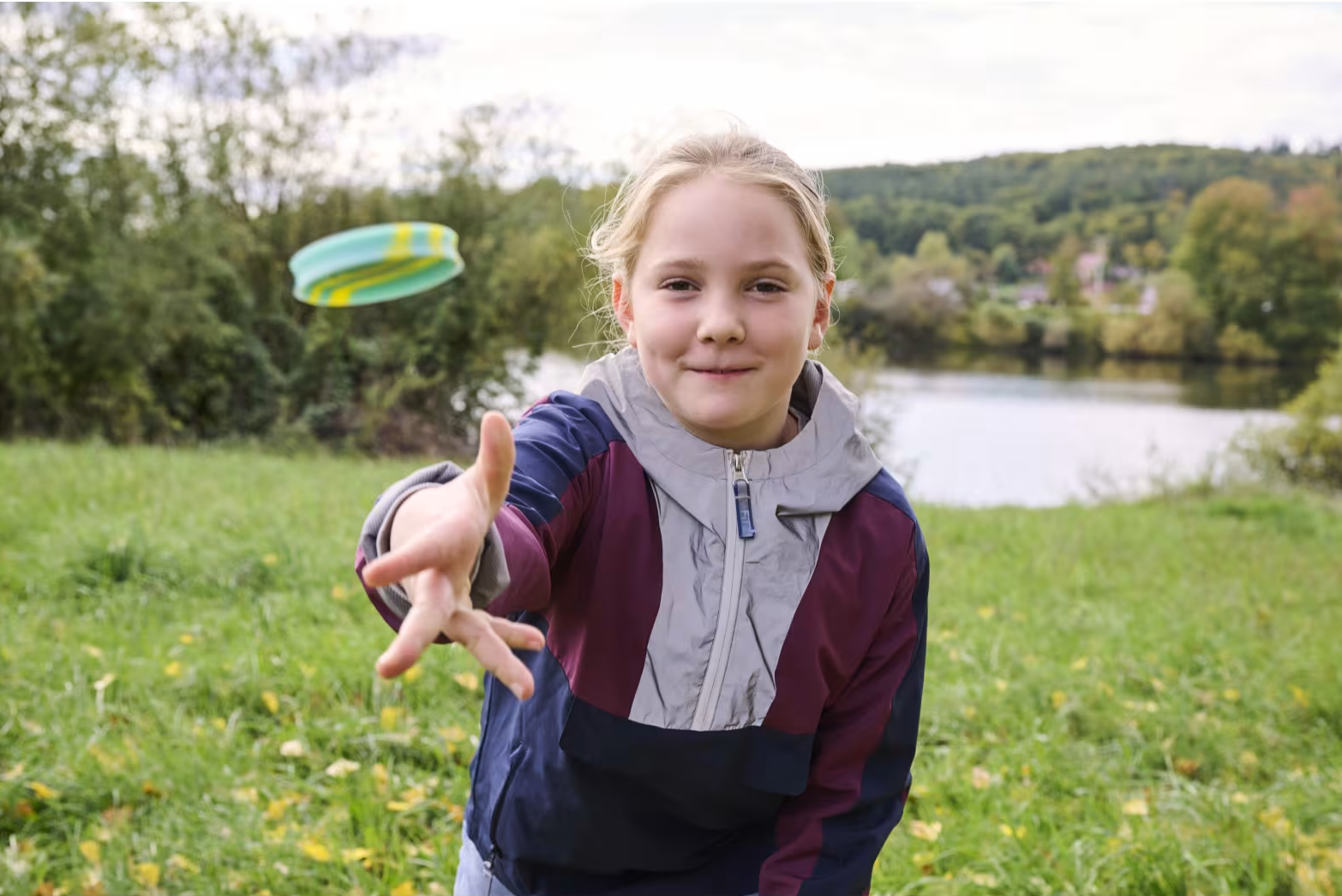 Egy lány frisbit dobál egy parkban, tóval a háttérben.