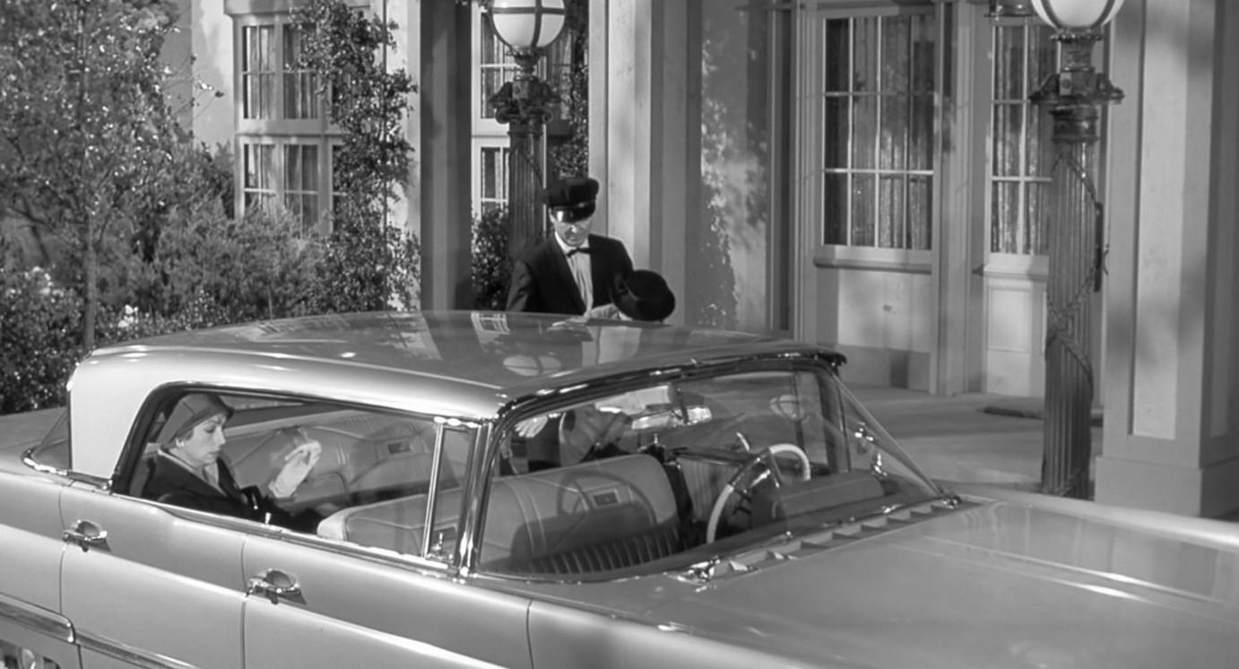 Ein Chauffeur hält einen Hut, während eine Frau im Auto sitzt.