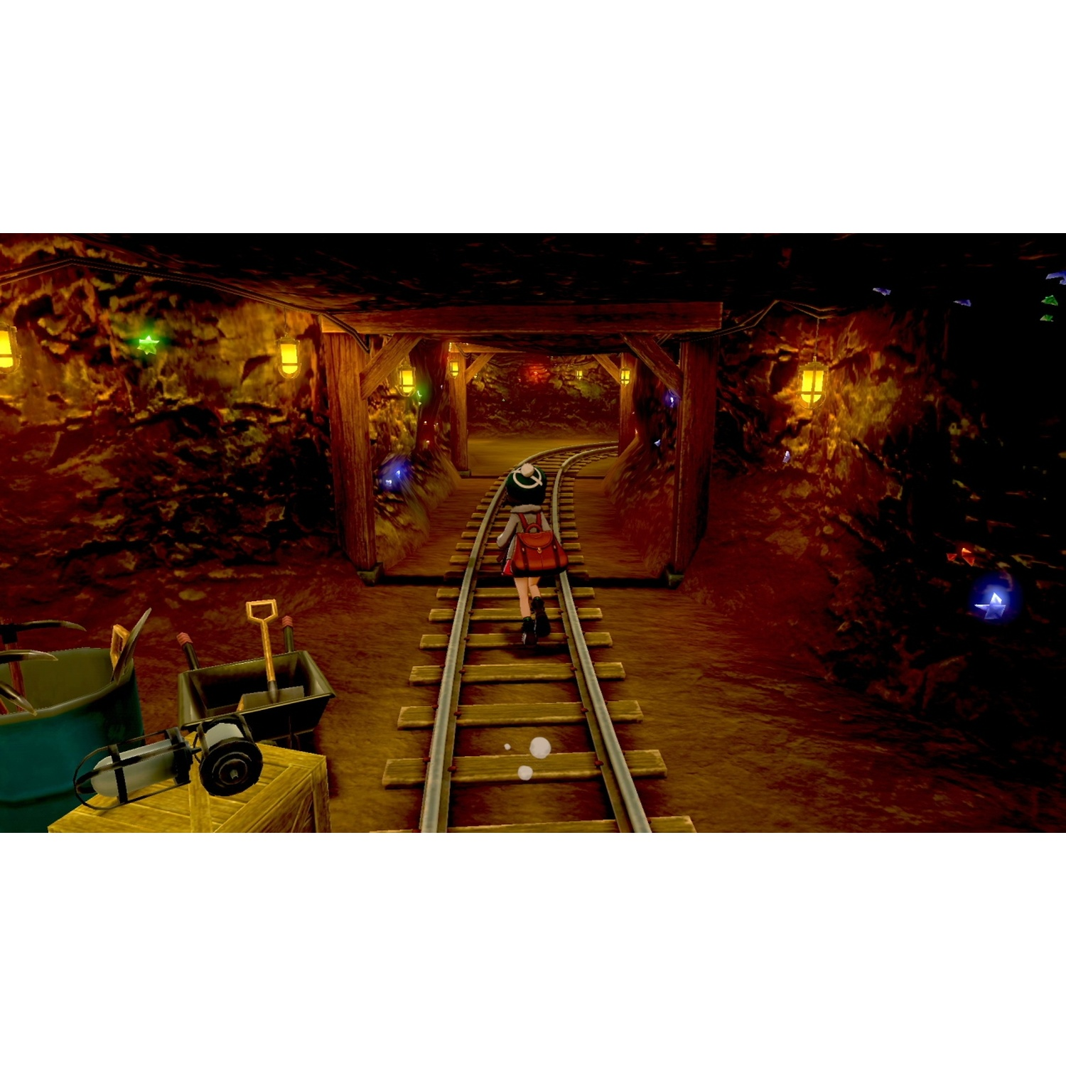 A person walks on train tracks in a lit mine shaft. Tools are on the left.